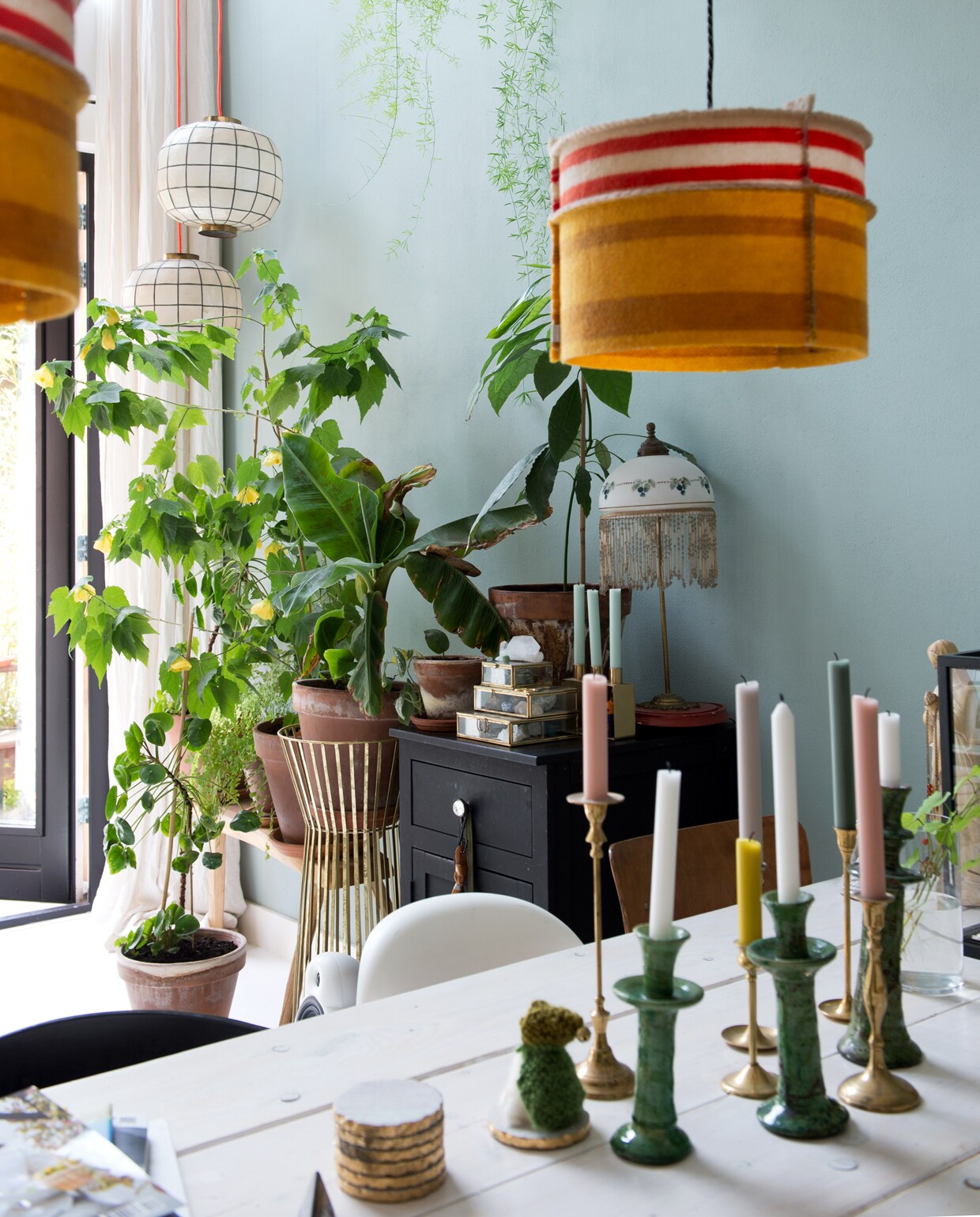 Tafel van Jorg Steigerhout. Erop een groene Tamegroute vaas en kandelaren van World of Blends. De bank hebben Jet en Michiel op maat laten maken bij oudisnieuw.net. Oranje kussen kelimshop.nl. Tulip Chair van Eero Saarinen en witte Panton Chair via Marktplaats. Hanglampen Woollight van beeldenbouwers.nl. Zwart geverfde oude commode. Glazen doosjes Sissy-Boy Homeland. Lamp met franje uit Antwerpen. Parelmoer met messing hanglamp ouders Michiel. Muurverf kleur Lianne van Fairf.