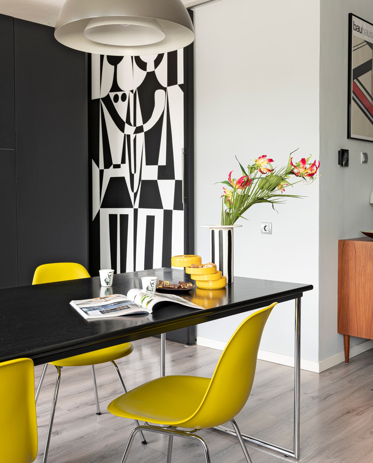 Muur zinkgrijs Karwei. Lamp Arne Jacobsen, tafel Gispen, gele stoelen Vitra Eames, kastje en gele bakjes Marktplaats. Vloer Ikea. Zwart-wit beschilderde schuifdeur zelfgemaakt. Vaas Loods 5, kopjes Il Coccio.