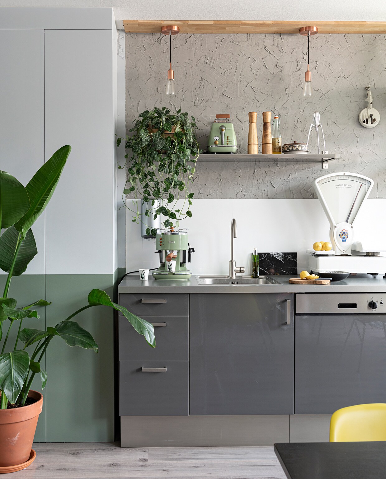 Muurkast zelfgemaakt, kleur zinkgrijs en leemgroen Karwei. Keuken en plankje Ikea. Achterwand keuken boerenstuc zelfgemaakt. Hanglampen Karwei. Op de plank: broodrooster De’Longhi via Mediamarkt, peper- en zoutstel Ikea, olijfolie supermarkt, potje met deksel kringloop, sinaasappelpers Alessi via Flinders. Aan de muur links: Plenty Easypull Dispenser via Blokker, rechts bonensnijder van de rommelmarkt. Weegschaal rommelmarkt, koffiezetapparaat Icona van Delonghi, kopje Il Coccio, marmeren plank Stoned, houten plank Xenos, zeeppompje Rituals. Plantenpot Intratuin.