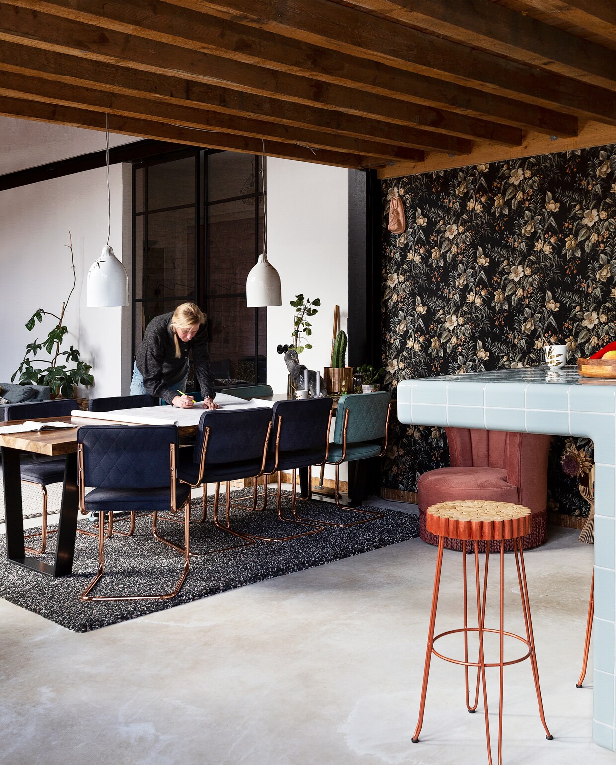 Eetkamertafel en stoelen Zuiver. Roze Dutchbone fauteuil Loods 5. Bufferlampen Pols Potten. Barkruk Kave Home Farley. Vloerkleed Ikea, behang Hornbach. Vloer van gevlinderd beton.