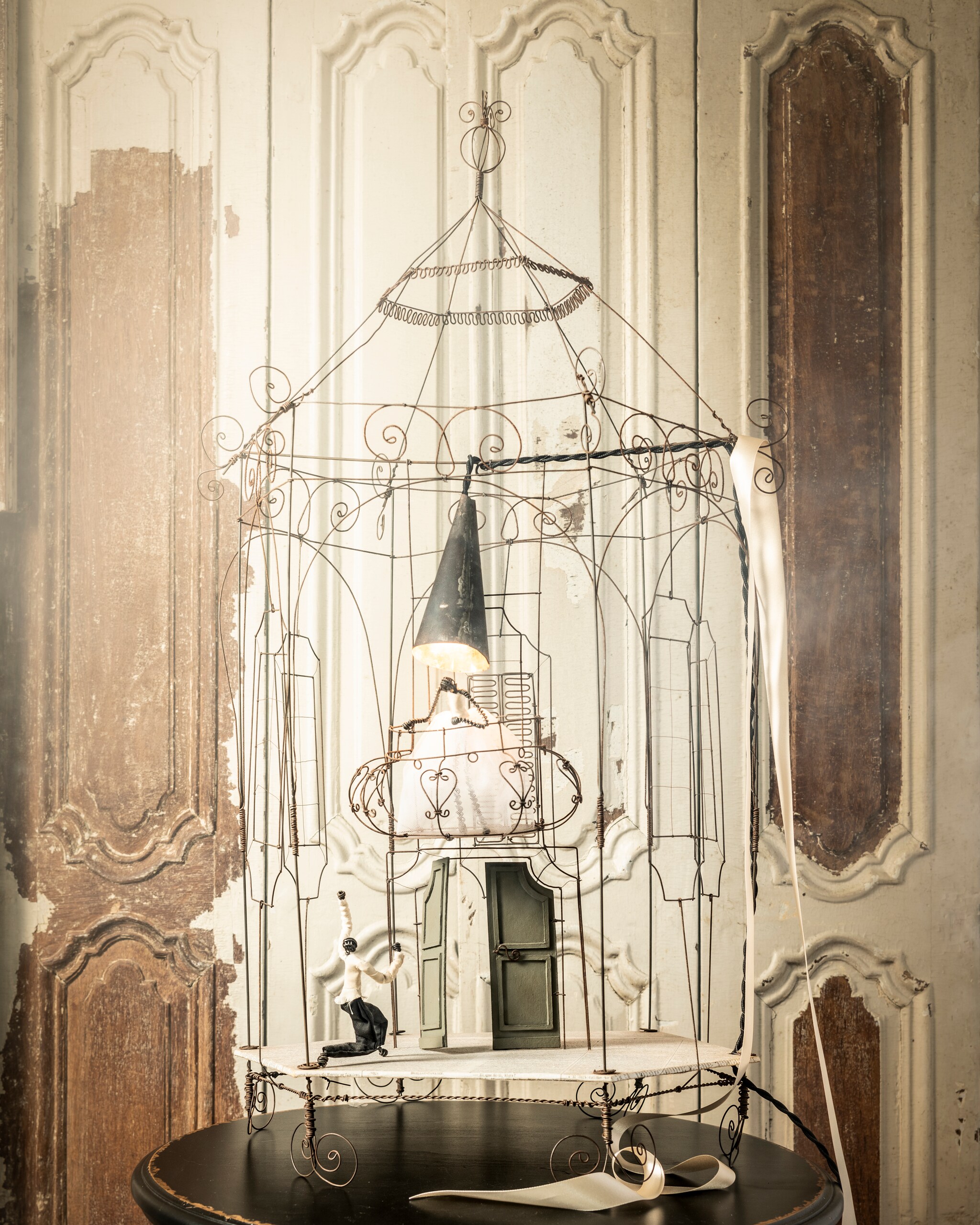 Handgemaakte lamp van ijzerdraad € 995,- (brechtmurreatelier.nl). Houten luiken per stuk € 175,- (burbri.nl). Bijzettafel € 85,- (harlequin-lisse.biz).
