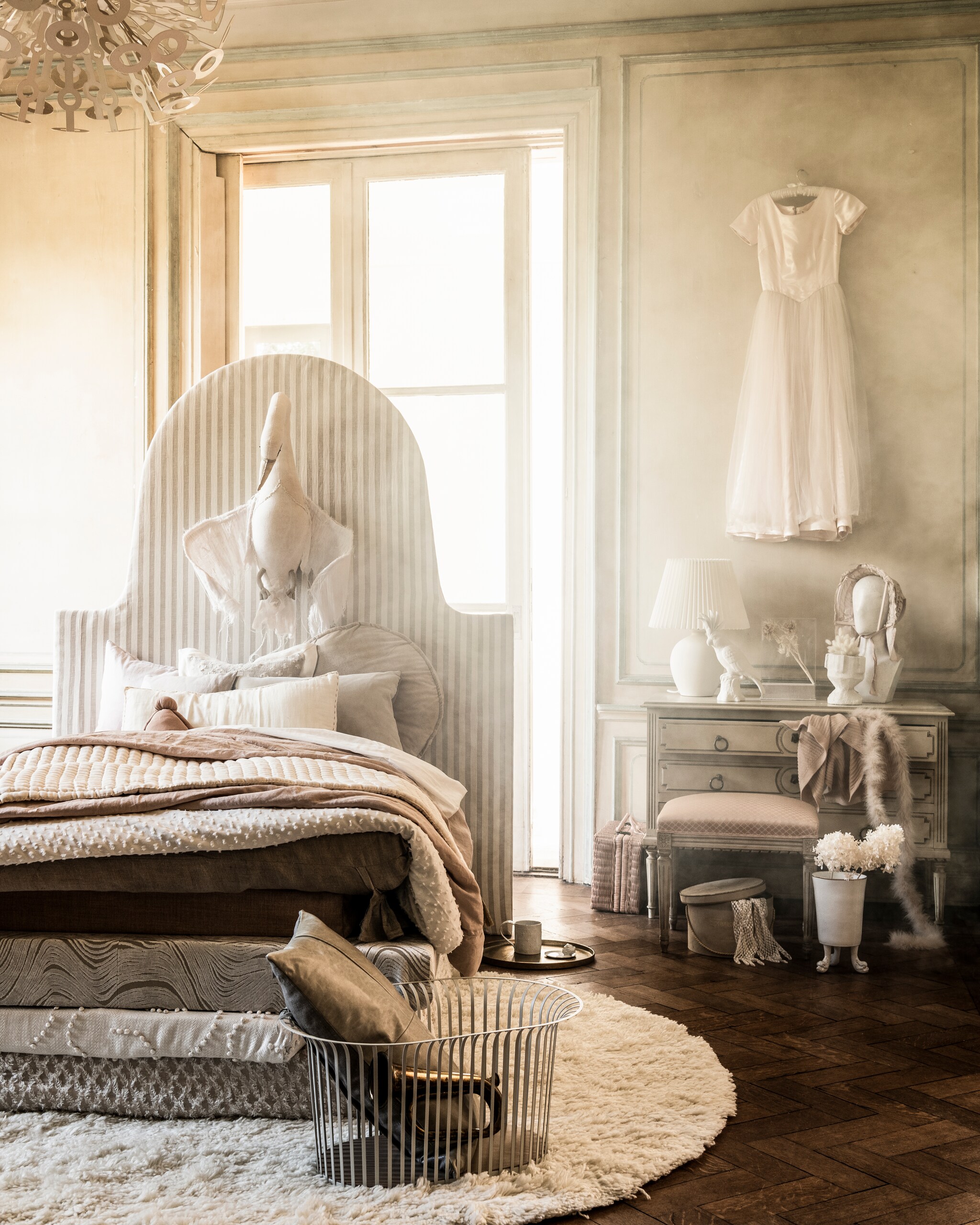 Matrassen en hoofdbord prijs op aanvraag (com-anders.nl). Stoffen op bed: linnen met streep Endless Summer Barbara Osorio per meter € 139,-, linnen in zalmkleur Valloire Designers Guild per meter € 85,-, linnen met golfmotief Aurelia Designers Guild per meter € 170,-, linnen met bolletjes Yotis Anatolia Nobilis per meter € 225,-,linnen met opengewerkt ruitmotief Kerouan Phoenicia Nobilis per meter € 104,-,linnen kussen met gaten Theia Nobilis € 238,-, langwerpig velours kussen € 88,- (wva.nl). Dekbedovertrek van wit plumetis € 69,99, zalmroze dekbedovertrek € 69,99, witte kap op schemerlamp € 29,99 (hm.com). Hanglamp privébezit. Rond kussen van HKliving € 64,95, rond kleed Vantaa van Linie Design 200 cm (Ø) € 495,-, gouden dienblad Palace van Salt &amp; Pepper € 39,95, witte kaketoe van Pols Potten € 59,-, vierkante stolp van HKliving € 89,95 (vtwonen.nl). Metalen mand € 210,- met daarin kussen € 135,-, kussen links op bed € 105,- (homestede.nl). Blaasinstrument € 20,-, hoedendoos € 35,- (harlequin-lisse.biz). Witte mok, per stuk € 99,-, schotel met hoofd erop € 75,-, vaas op pootjes € 332,- (maisonnl.com). Droogbloemen (judithslagter.nl). Vintage jurk € 225,-, lange handschoenen € 15,-, verenslinger € 45,- (lauradols.nl). Hoofd met hoed € 150,- (prinsheerlijkantiek.nl). Ladenkast € 325,- (burbri.nl). Kruk € 65,- (vandijkenko.nl). Rieten koffer € 85,-, zwaan € 595,-, roze knuffel in bed € 45,-, langwerpig kussen € 22,-, wit plaid € 90,-, zalmkleurig plaid uit ladekast € 90,- (archive-store.nl). Handgemaakte, witte vaas op kast prijs op aanvraag (babetteswereld.com).