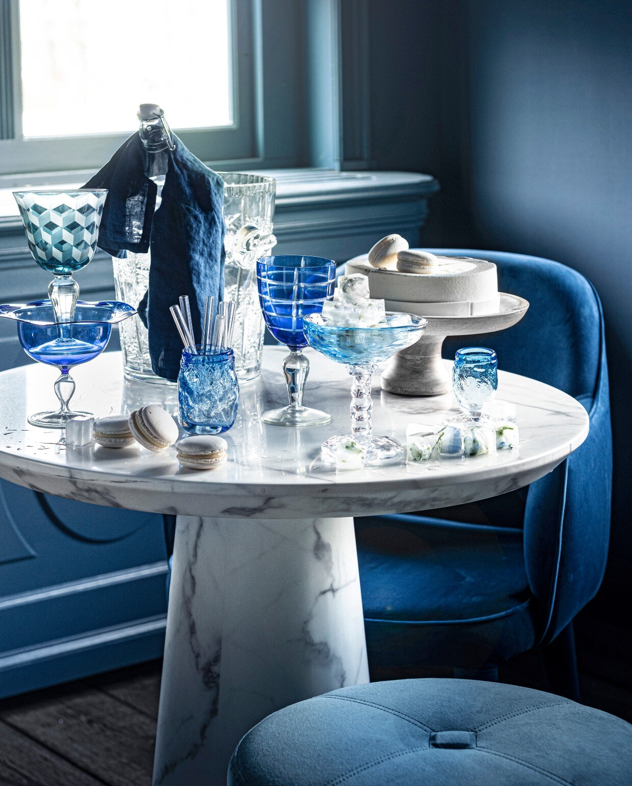 Poef van Minotti € 1150,-(covanderhorst.nl). Stoel Cosy van PolsPotten € 302,99 (vtwonen.nl). Wijnkoeler€ 175,- (pietjonker.nl). Blauw wijnglasmet print links, set van 6 € 129,-, blauwgestreept wijnglas in het midden, set van 6€ 129,- (polspotten.nl). Waterkaraf metdop, prijs op aanvraag (sostrenegrene.com).Blauw glas linksonder € 10,- (loods5.nl).Glazen rietjes, set van zes € 10,50(bijenkorf.nl). Taart gemaakt naar wens€ 32,95 (huizevanwely.nl). Gebobbeldglas € 30,-, gebobbelde ijscoupe metijsklontjes € 50,-, smal gebobbeld blauwglas € 20,-, linnen servet, set van 2 € 9,99(hm.com). Zelfgemaakte ijsklontjesmet blaadjes en bloemetjes erin. Overigprivébezit.
