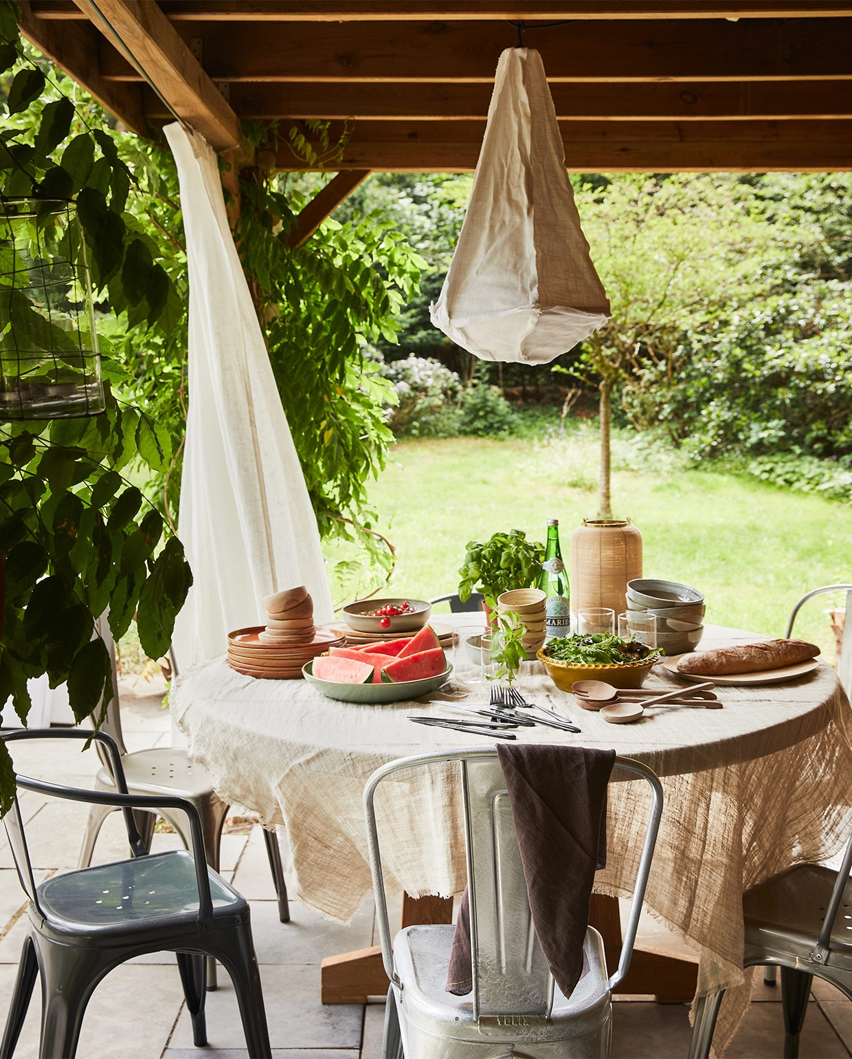 Teakhouten tafel, 140×75 cm (Øxh), kommen, diepe borden, platte borden, grote kommen met penseelstreek (hkliving.nl). Metalen stoelen (extravert.nl). Gordijnen Hilja, 145×300 cm (ikea.com). Hanglamp Torch, 40×64 cm, tafelkleed van HKliving 150×250 cm, bruine linnen theedoek van vtwonen (vtwonen.nl). Olijfkleurige schaal, walnoten saladeset (householdhardware.nl). Rest privébezit.