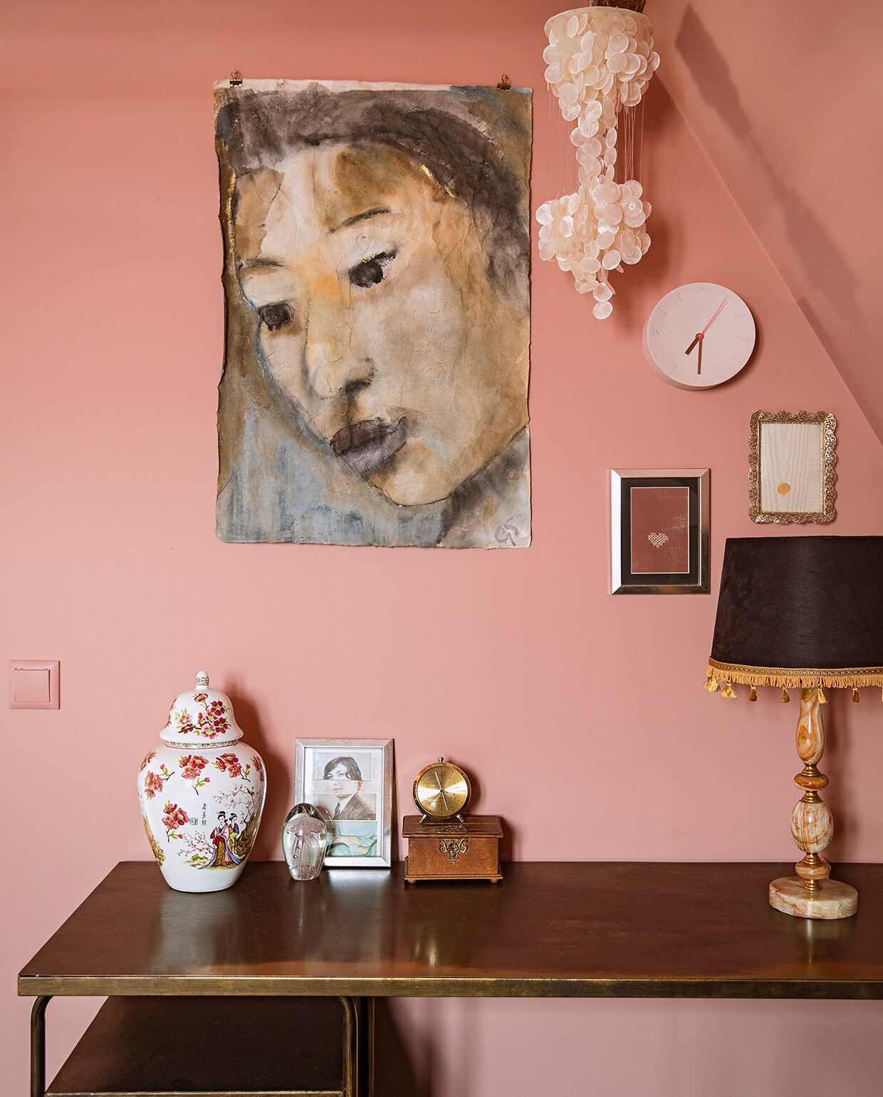Muurverf Rosewood van Painting The Past. Sidetable BePureHome. Aardewerken pot, kwal in glas, gouden wekker en hangend schelpenornament herkomst onbekend. Ingelijste foto uitgeknipt uit tijdschrift Flow. Kistje en fotolijstjes erfstukken. Portret op doek Grace Spiegel. Wandklok Studio Harm en Elke. Zelfgemaakte tafellamp van tweedehands voet en gecustomized kap.