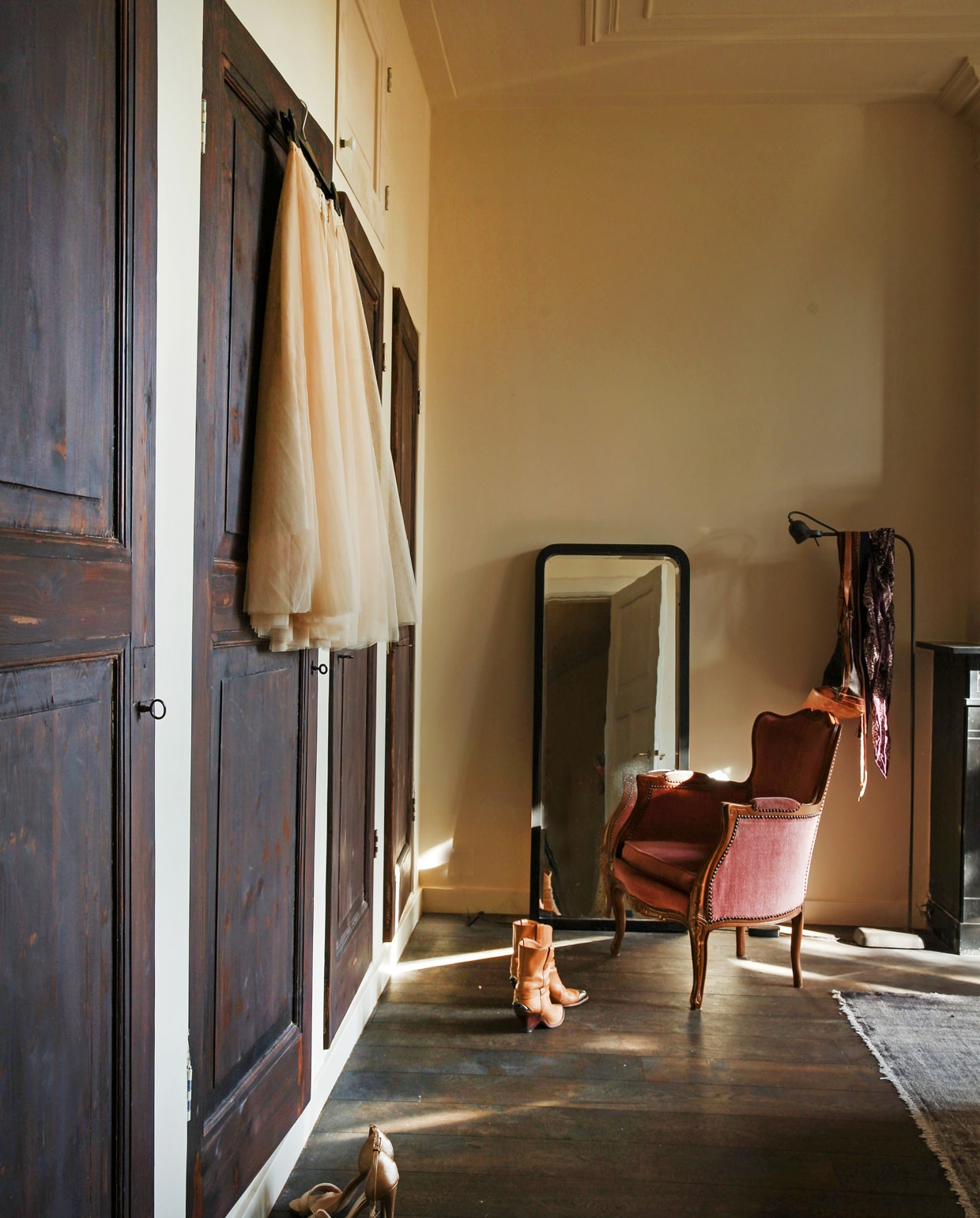 Achter het behang in de slaapkamers op de verdieping zaten blinde deuren verstopt. Nieuw opgeschuurd werden het de deuren van opbergkasten. Vintage spiegel, vloerkleed en fauteuil. Vloerlamp Brecht Murré Atelier.
