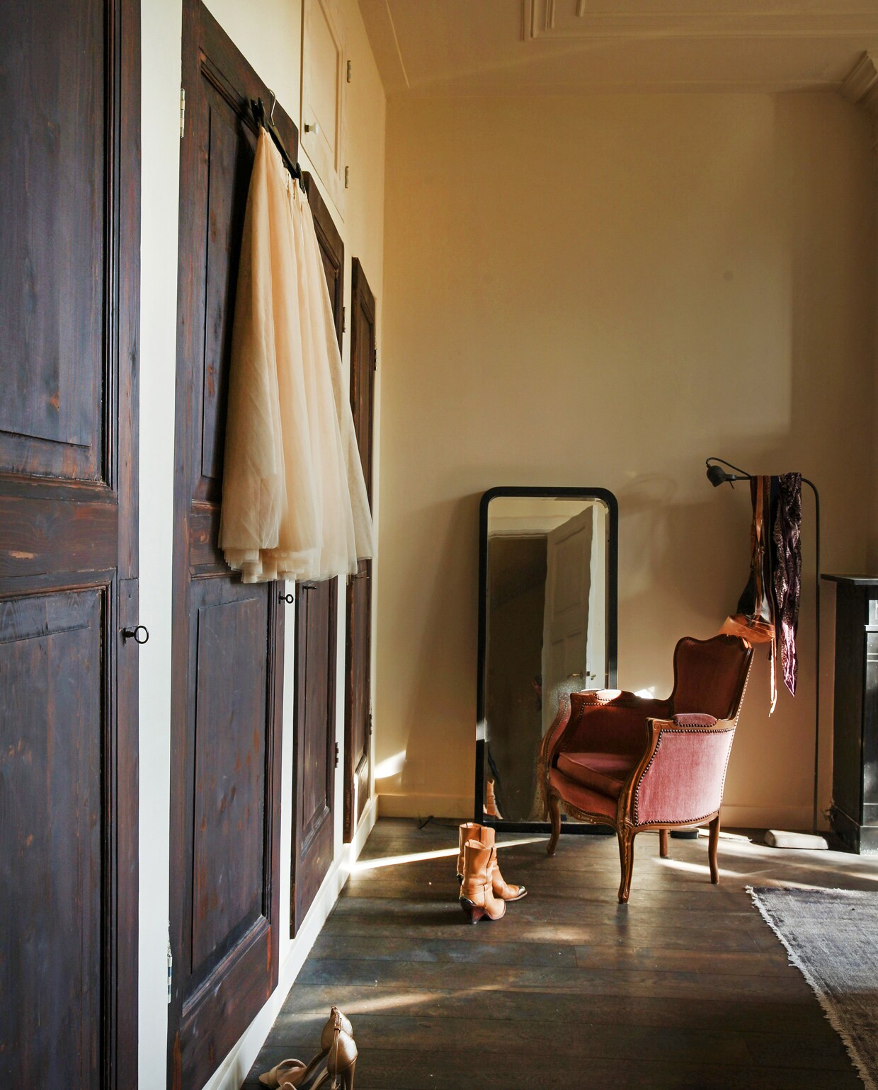 Achter het behang in de slaapkamers op de verdieping zaten blinde deuren verstopt. Nieuw opgeschuurd werden het de deuren van opbergkasten. Vintage spiegel, vloerkleed en fauteuil. Vloerlamp Brecht Murré Atelier.