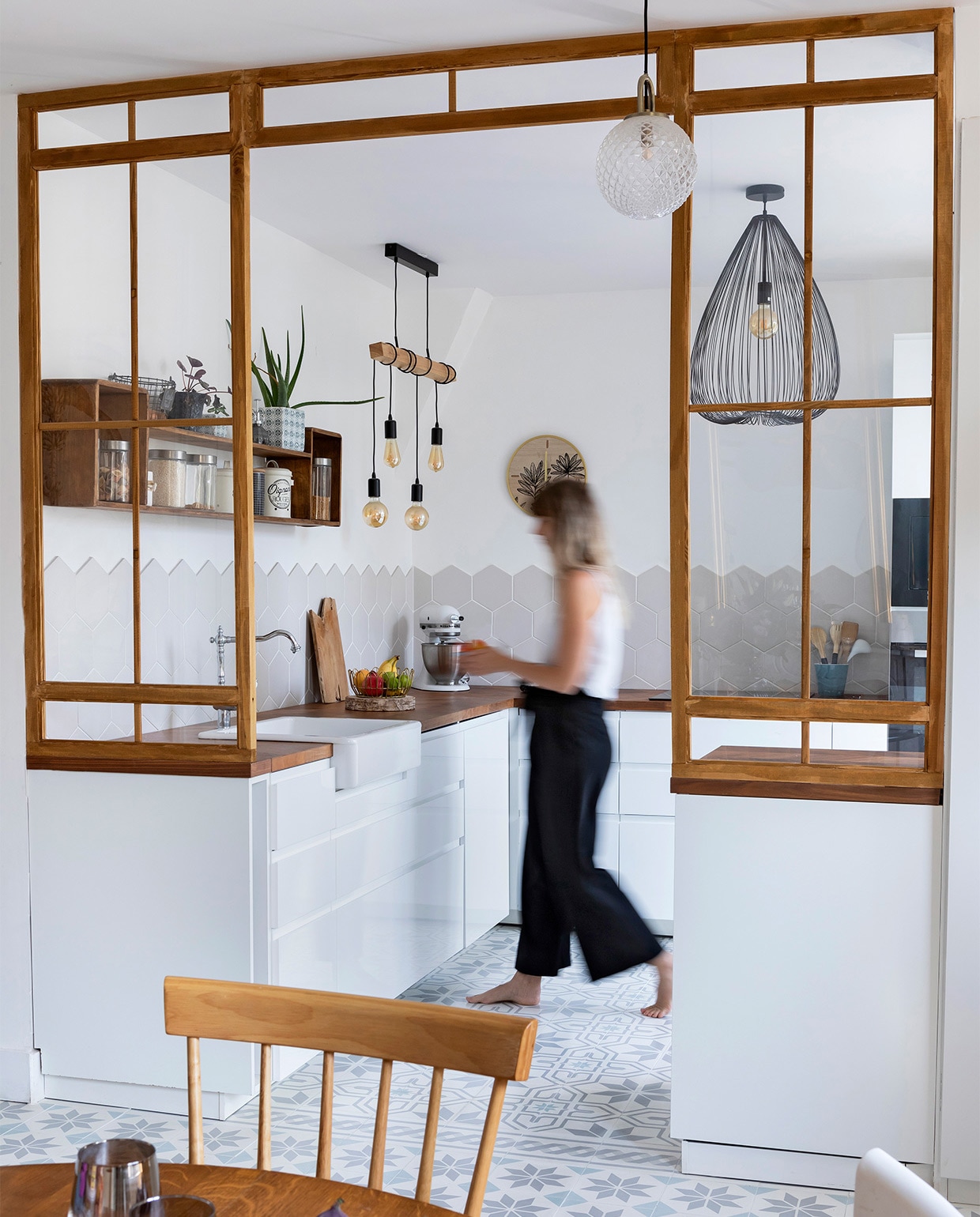 Het rechte aanrecht werd vervangen door een L-vorm en een keukeneiland bij de ingang. Vloertegels Mosaic del Sur. Wandtegels asdecarreaux.com. Keuken Ikea. Houten wandkast tweedehands. Peertjes aan houten balk Leroy Merlin. Zwarte plafondlamp Alinea. Overig onbekend.