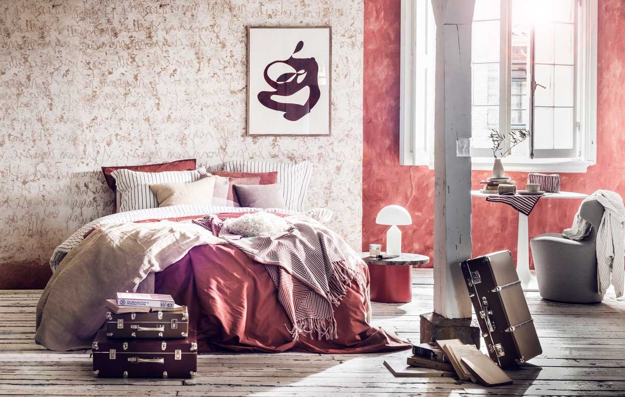 Muurverf kleur Drummond 16 van Little Greene,  (De Ru). Behang met letters, prijs op aanvraag (Wall&amp;decò). Beddengoed wit met grijze streep  rood beddengoed , sprei wit met rode streep 130×170 cm, geblokte kussenhoes, 50×50 cm  grijs-witte linnen japon H&amp;M Home). Zandkleurige sprei, 130×170 cm , kussen, 50×50 cm  (Zara Home). Grijs kussen, 40×40 cm (Bolia). Ronde bijzettafel Enoki gebruikt als nachtkastje , witte lamp -(Mobilia). Toilettas rood met witte strepen rood-wit handdoekje op tafel  (Anna + Nina). Witte tafel met afgeronde randen  grijze stoel - (Edha interieur). Schotels per stuk, kom  vaasje (Annemieke Boots Ceramics). Koffers vanaf- (Archive Store). Boek The Monocle Guide to Drinking &amp; Dining (Six and Sons). Kunst aan de muur (Cate Adriana). Overig privébezit.