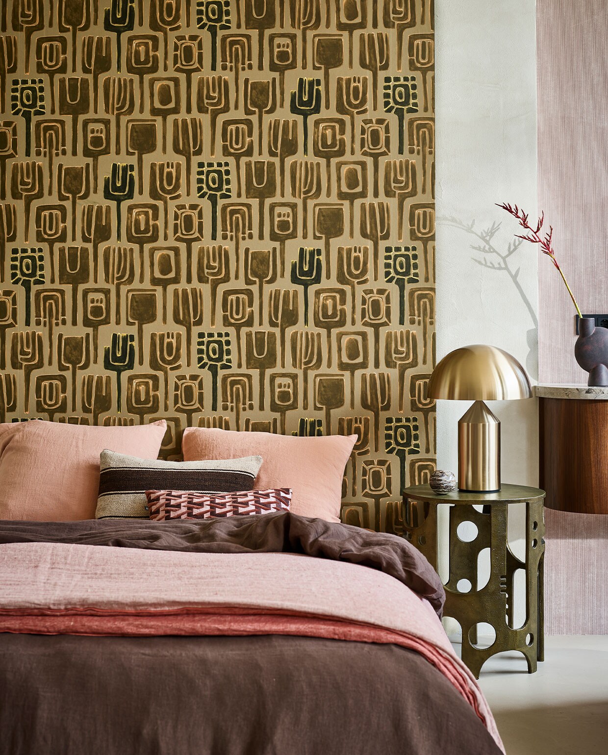 Behang Totem TP31001 van Élitis, 1000×70 cm per rol € 174,- (loggerewilpower.com). Goudkleurige bijzettafel € 887,50 (versmissen.nl). Goudkleurige tafellamp Atollo van Oluce, € 1126,25 (homestede.nl). Bruine ronde vaas Sphere € 40,50 (casagitane.com). Donkerbruin linnen dekbedovertrek, 220×240 cm € 325,-, kussenslopen, 65×65 cm per stuk € 39,-, rozerode deken Cocoon Vice Versa, € 550,-, gestreept kussen, 50×30 cm € 125,- (couleurlocale.eu). Roze/bordeaux kussen, 30×40 cm € 49,95 (hkliving.nl).