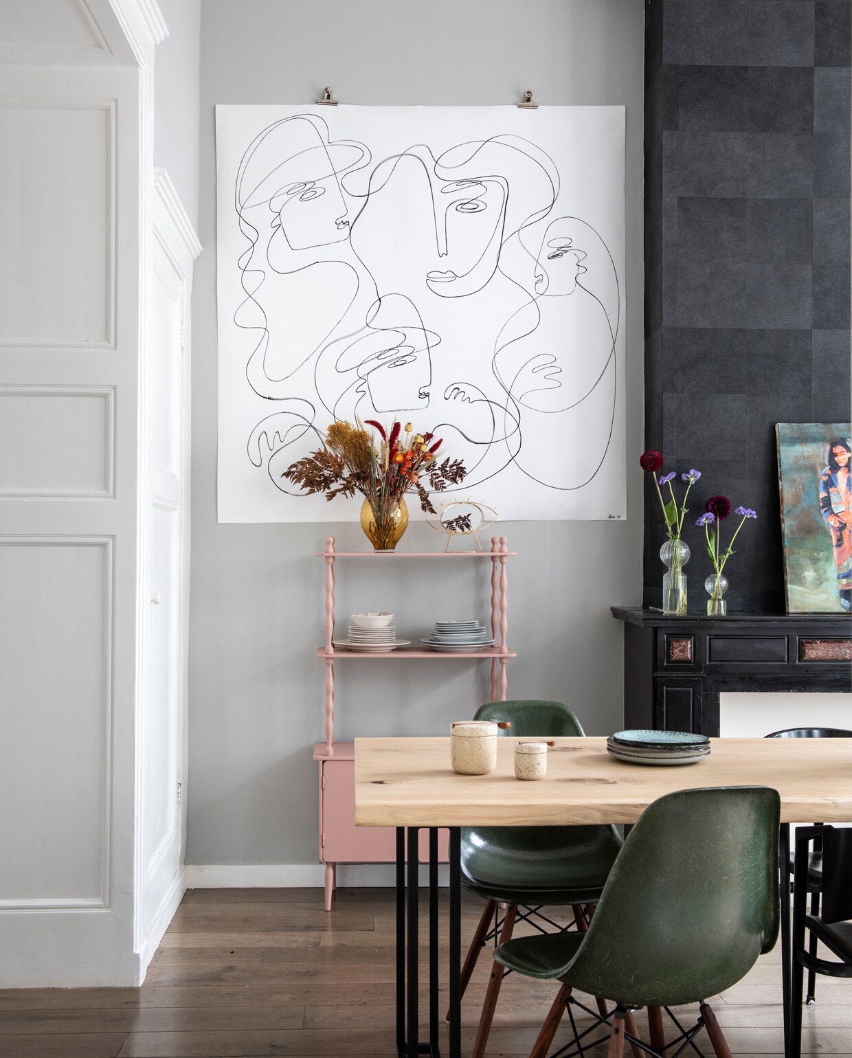 Aan de muur hangt een werk uit de collectie Entangled van Anne Mei Poppe. Eiken eettafel van Wdstck, vintage Eames fiberglass stoelen van The Modern (modernvintage.nl), vintage kastje van All the Luck in the World. Droogbloemen van Aimelie. Het zwarte behang is nog van de vorige bewoners. Vaas op de kast cadeau gekregen, overige vazen &amp;klevering. Borden ‘van oma’ en tweedehandswinkels. Potjes H&amp;M. Op de schouw: kunst van Jasper Krabbé.