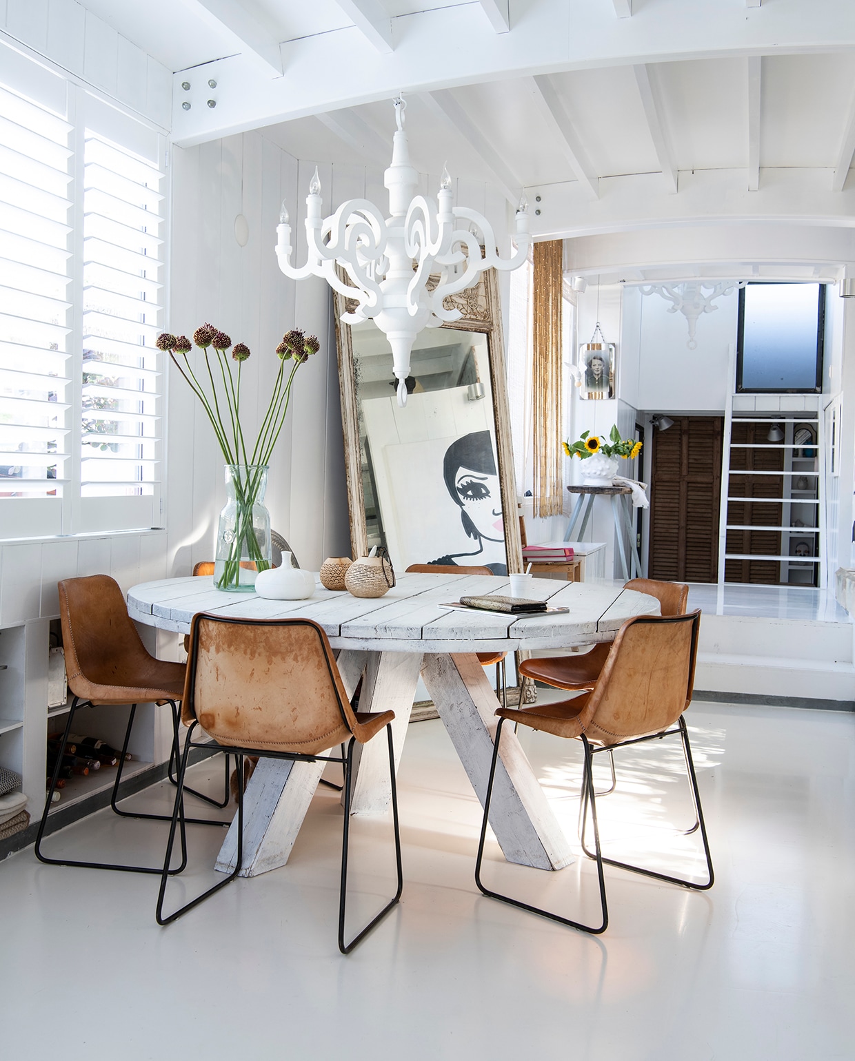 Ronde wit gebeitste houten eettafel Marktplaats, stoelen Giron met leren zitting Sol y Luna, erboven Paper Chandelier van Studio Job voor Moooi. Grote vaas, merk onbekend, witte vaas Couleur Locale in Knokke. Kalebassen op tafel Sukha. Grote spiegel vintage.