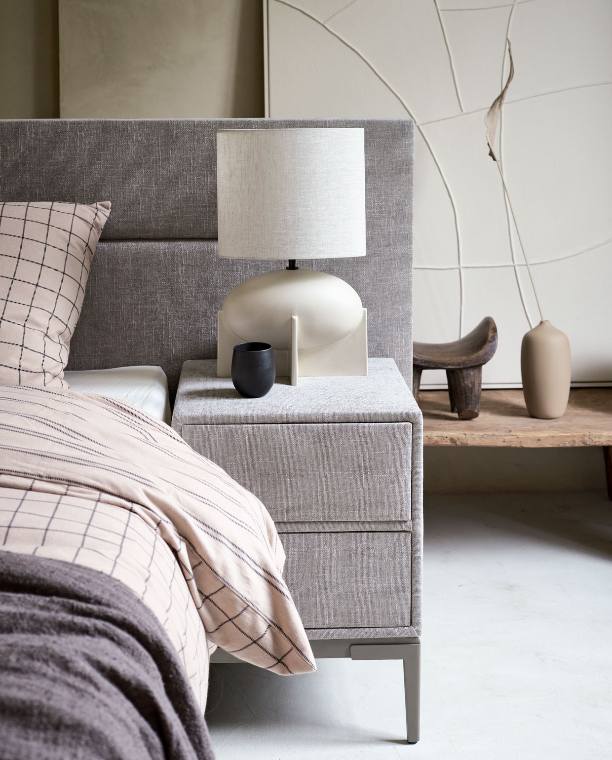 Boxspring Lifestyle by vtwonen Cinnamon Large vanaf € 1750,- (140×200 cm), nachtkastje Cardemom met twee lades, 45x45x62 cm (lxbxh) vanaf € 199,-, verkrijgbaar met verschillende stoffen en kleuren. Hier uitgevoerd met stof Mirage Taupe, metalen frame in kleur Champagne en poot Track. M.m.v. allestedlund.com (lamp), nordal.eu (grijze linnen plaid, kan en beker, marmeren schaal, linnen kussen), vtwonen.nl (zandkleurige vaas, beddengoed Grid in kleur zand uit de vtwonen collectie).