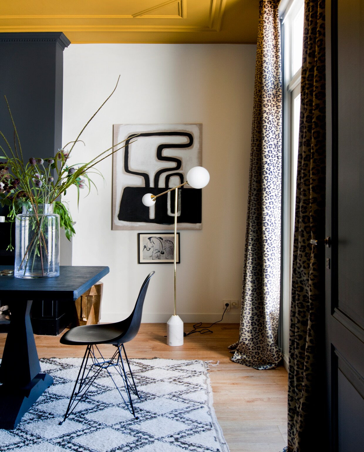 Eetkamer met spectaculair plafond in Lush Mustard van Flexa. Tafelverf: Off-Black van Farrow &amp; Ball. Het kunstwerk op linnen is gemaakt door mijn moeder.’ Lamp made.com, kunstwerkje HK Living, stoel DSR van Eames (Vitra), vintage berber uit Marokko. Vaas is een cadeau. Stoop Interieur leverde de velours stof met luipaardprint voor de gordijnen.