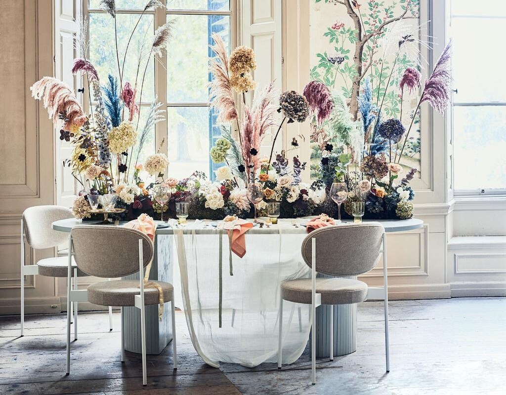 Bloemenloper prijs op aanvraag (edenique.nl). Tafelkleed gemaakt van kaasdoek per meter € 2,- (boerenbonthal.nl). Stoelen van Verpan vanaf € 732,- (dezaakdesign.nl). Ovale tafel, op maat gemaakt, 220x110x76 cm vanaf € 750,- (com-anders.nl). Waterglazen € 7,95, goudkleurig bestek € 49,25, diner­borden € 21,95, mintgroene borden € 14,50 (vtwonen.nl). Servetten € 6,20, roze wijnglazen met goudkleurige rand € 9,65 (nordal.eu).
