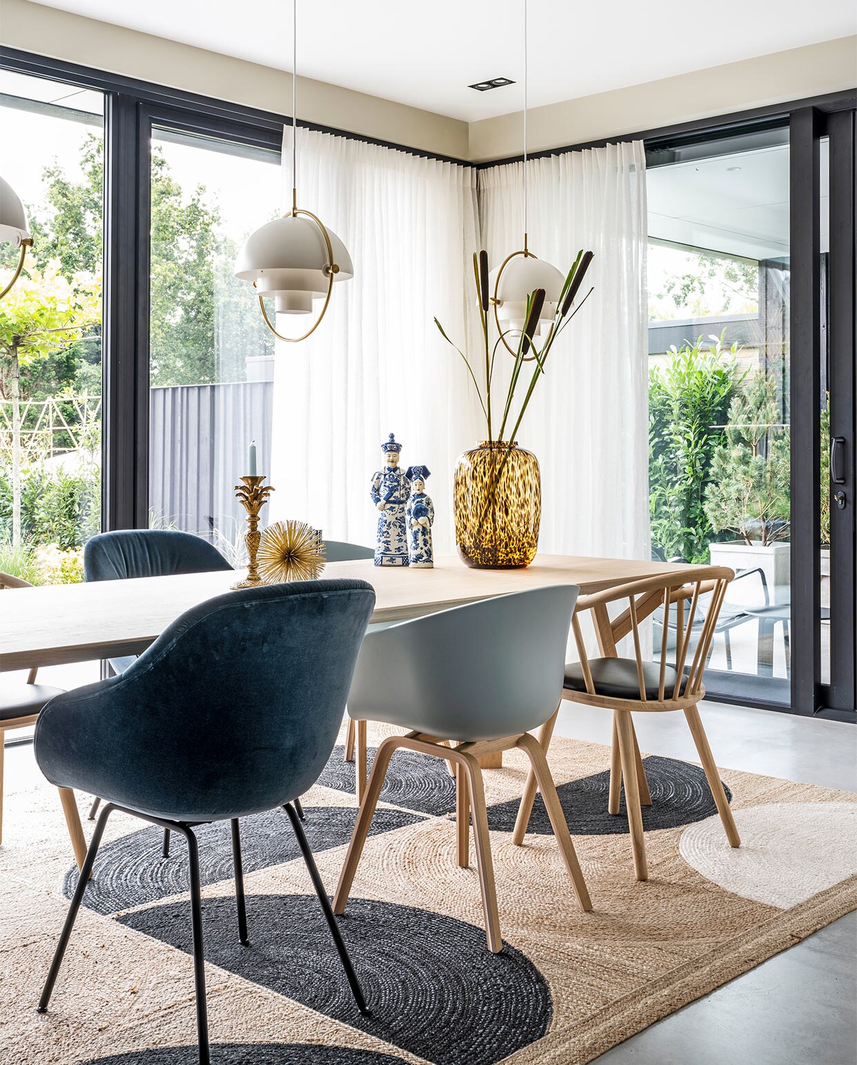 Hanglampen Multi-Lite Gubi, tafel Arp Design, vloerkleed Élitis, donkerblauwe en lichtblauwe stoelen Hay, houten stoelen zwarte zitting Bolia, gouden stekelitem Loods 5, kandelaar palmboom Anna+Nina, beelden Asian Mix Interior, vaas Artic Cheetah Vase the World, linnen gordijnen Interstil.