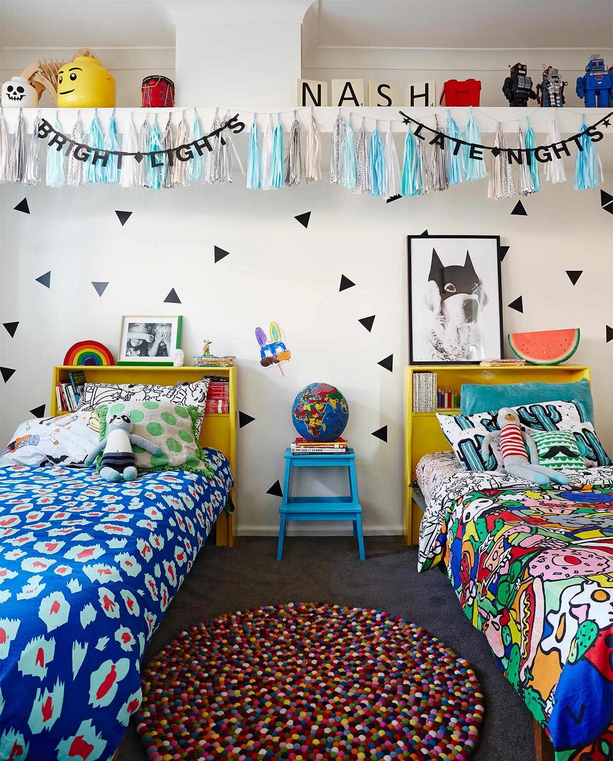 Muurstickers Urban Wall. Gele bedden gekregen van Hayleys tante, die er als kind in sliep. Dekbedovertrek rechts en zwart-wit kussen Kip &amp; Co. Trapje Bekväm Ikea, zelf blauw geverfd. Wereldbolkussen Hugg-a-Globe. Print Batdog My Dear Art Shop. Kwastenslinger DD Brand. Wit en geel opberghoofd Lego. Overig onbekend.