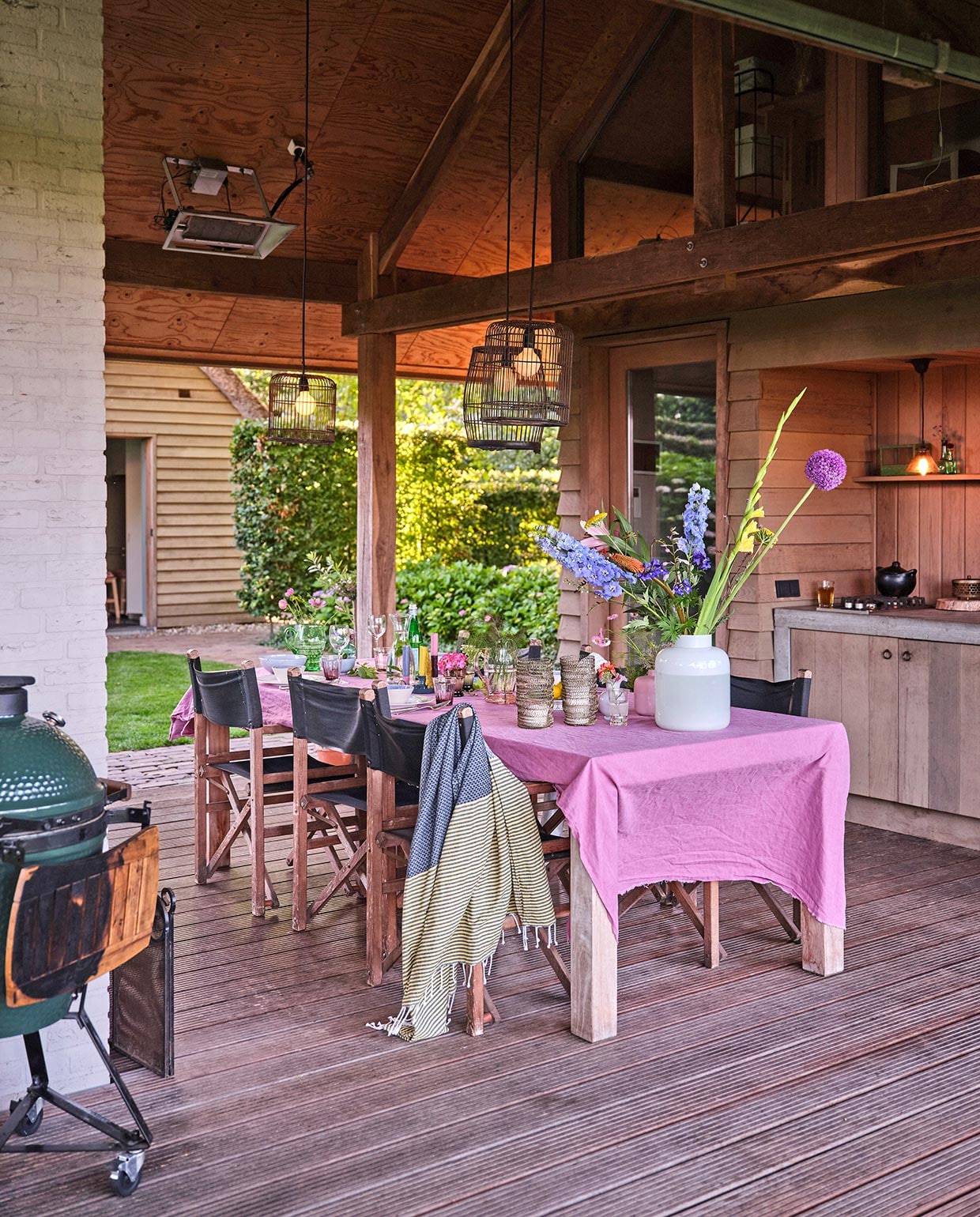 Keuken in tuinhuis zelfgemaakt van wrc-delen, rode ceder. De lampen zijn vogelkooien die zwart gespoten zijn. Het roze tafellaken is een onafgewerkte linnen lap van de markt. Barbecue Green Egg. Hammamdoek Sissy-Boy Homeland. Regisseursstoelen Vervoort Meubelen.