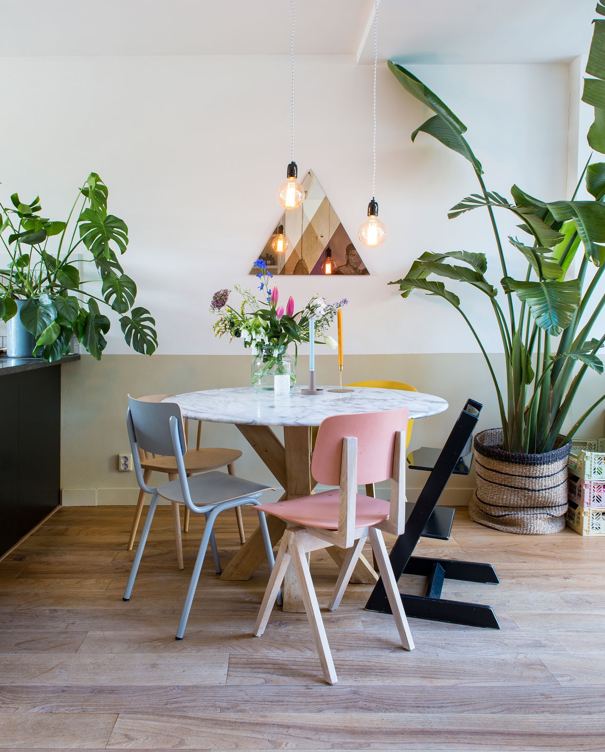 Eettafel met marmeren blad van Marktplaats, eikenhouten kruispoot gemaakt door een timmerman. Roze stoel Galvanitas en grijze stoel Back to School van Zuiver via Loods 5, houten stoel J104 en gele stoel AAC22 van Hay, zwarte Tripp Trapp stoel Stokke. Transcience spiegel Lex Pot, lampen Bailey, mand Sissy-Boy, planten Strelizia Nicolai Primavera en Monstera, kratten Aykasa. De vloer is van lokaal iepenhout.