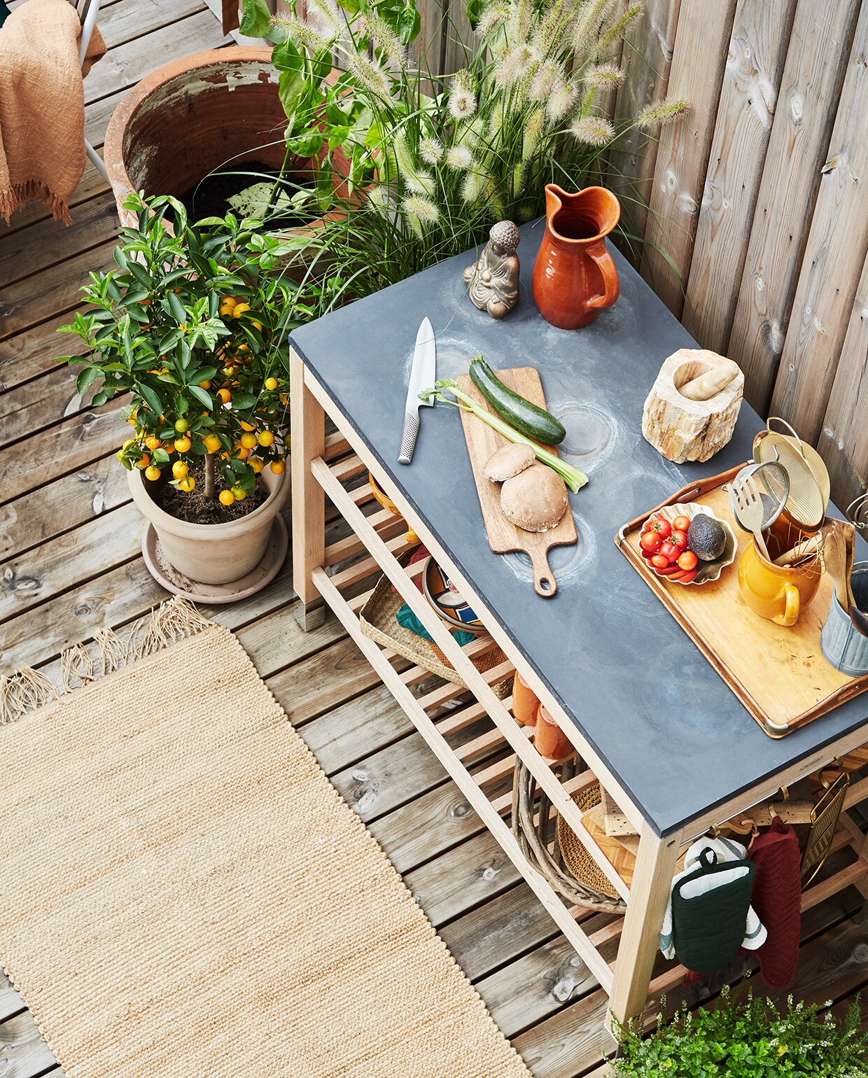 Deze buitenkeuken is van Skagerak en heeft een stenen aanrechtblad. Het terracotta servies matcht met de potten op het terras, waardoor de open keuken onderdeel van het geheel wordt. Het juten vloerkleed maakt de sfeer helemaal af. Dit kleed is van H&amp;M home.