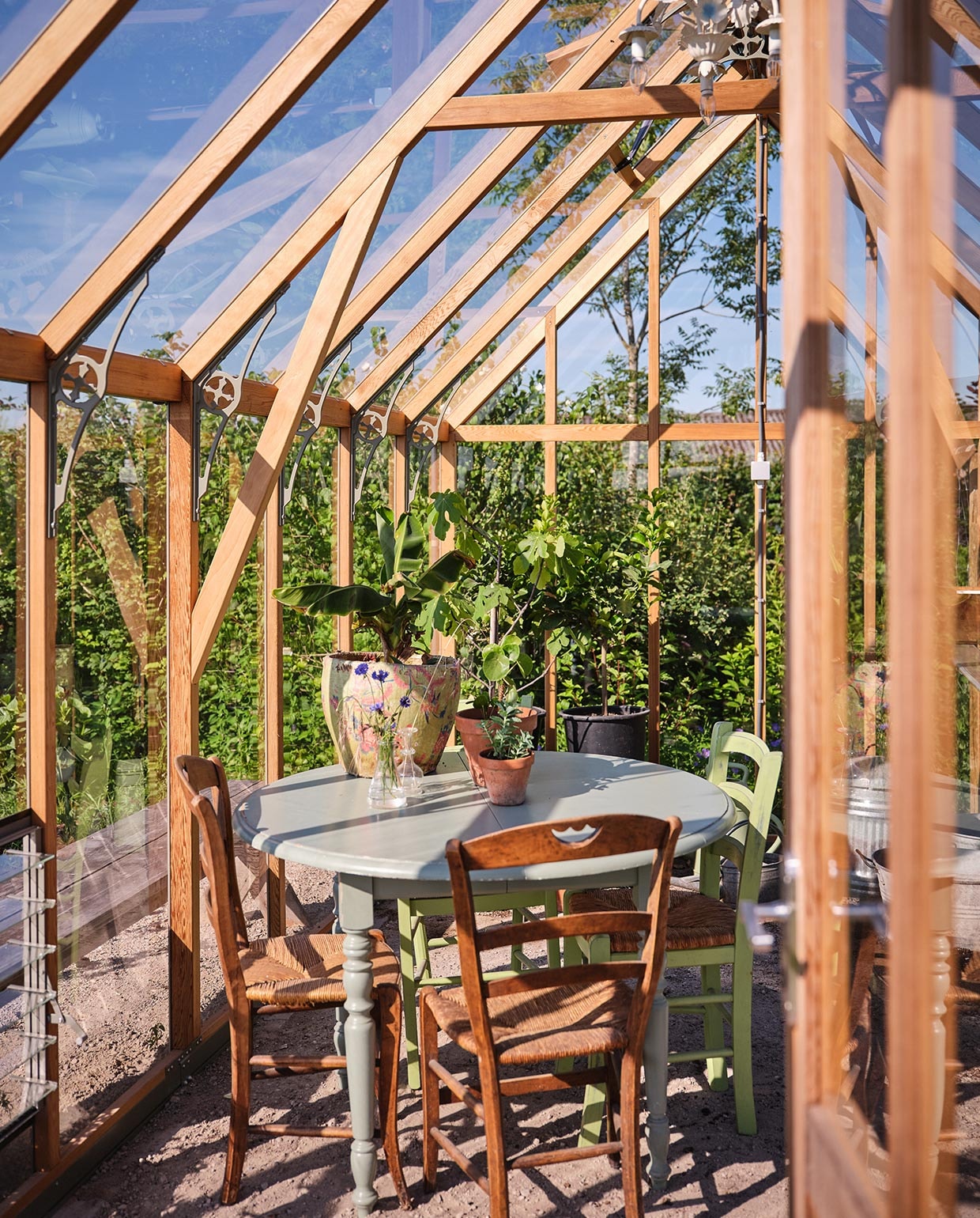De kas is van Alton en kwam in een bouwpakket via de Tuinkassenwinkel. Erin: een antieke tafel uit Frankrijk, geverfd in een zachtgroene kleur. De antieke stoelen eromheen komen ook uit Frankrijk.