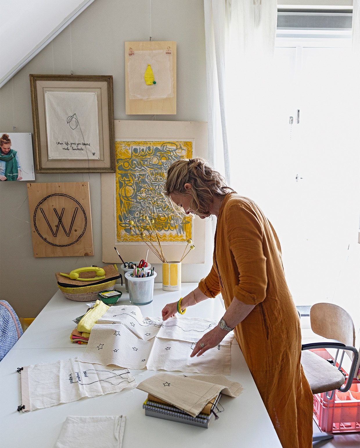 Karen in haar werkkamer op de eerste etage. Eames-tafel Vitra. Potten Rivièra Maison. Gele vaas gekocht bij een sociale werkplaats. Mand meegenomen uit Zuid-Afrika. Telefoonhoorn Native Union. Aan de muur hangen (met de klok mee) een citroenkunstwerk dat Karen maakte van plastic afval, een werk van Antoinette Gispen, het beeldmerk van Lemonwise (de W) en een geborduurde leus: If life gives you lemons, make lemonade. Foto visual merchandising Lemonwise. Stoel Marktplaats.