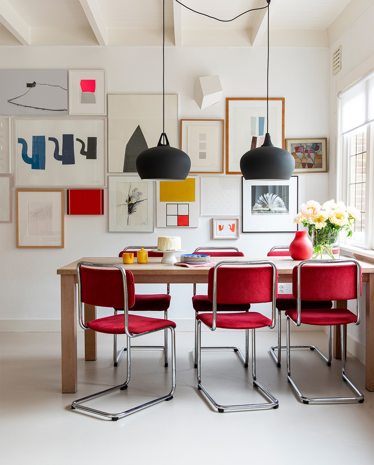 Kunst van onder anderen Albrecht Schnider, Fons Brasser, Alexander Schleber, Jaap Stellaart, Klaas Gubbels, Károly Keserü, Ko Oosterkerk, Reinhard Vrba (Nora’s vader), Hiroshi Harada, Anne Marie Lecluyse en Klaus Staudt. Op tafel vintage melk-en-suikerset, borden Dibbern, vaas Menu, taartplateau Dille &amp; Kamille. Lampen Belly 38 van Nordlux, stoelen Gispen, op maat gemaakte eettafel Jacco Bakker.
