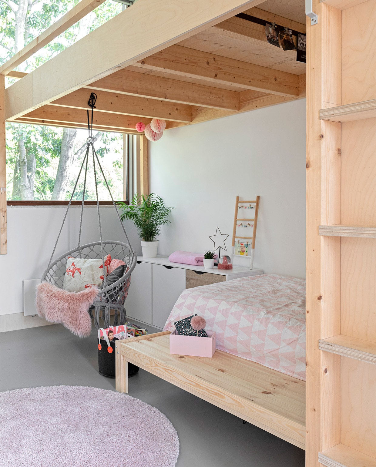 Entresol gebouwd door aannemer Klomp. Bed Ikea. Ladekast Leen Bakker. Een van de hangplekken: Hangstoel Xenos. Vissenkussen Raaf. Houten roze bakje Flying Tiger. Op de vloer linoleum Walton van Forbo. Pompons, zwarte mand Hema. Ladder Søstrene Grene. Overig onbekend.