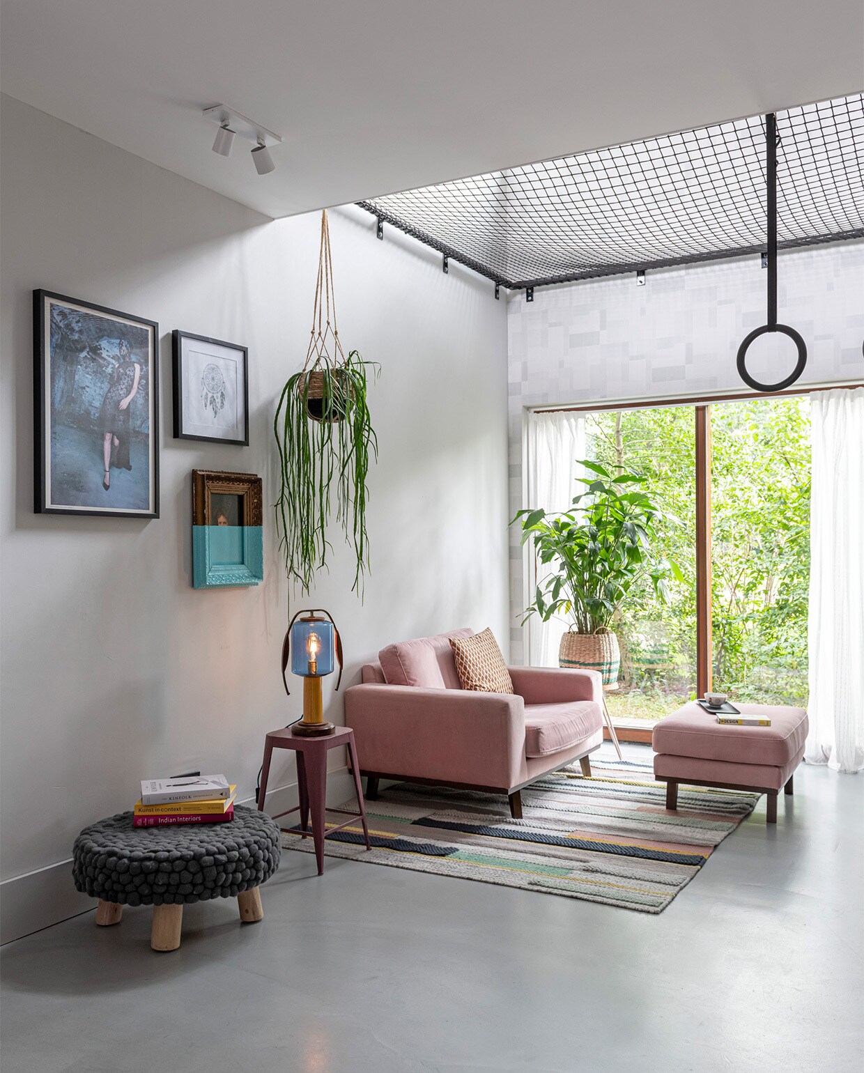 In de woonkeuken met vide hangt een vangnet in een stalen frame, gebouwd door bouwbedrijf Klomp. Net van Van Beelen NTN. Ultratop vloer in betonlook, behang op muur rond raam Norrköping van Engblad &amp; Co. Plafondspot Epic van Maretti. Fauteuil en voetenbank Wehkamp. Vloerkleed Ikea. Poef Loods 5. Aan de wand een ingelijste foto uit boek Sumo van Helmut Newton. Half geverfd schilderij kringloopwinkel. Prent dromenvanger rommelmarkt. Tafellamp Vintkracht Lichtobjecten. Zwarte ringen Bol.com. Manden Tuincentrum Overvecht. Bijzettafels Søstrene Grene.