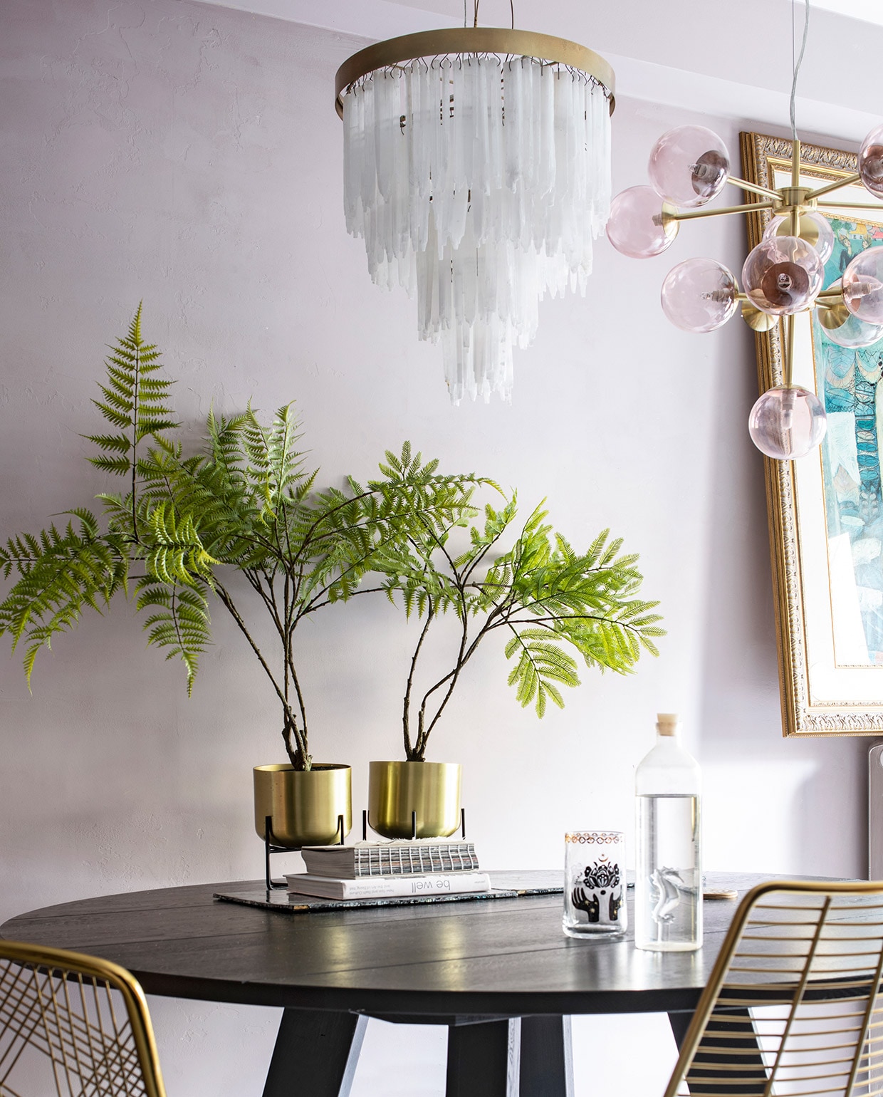 Ronde tafel van Leeelijk, de messing stoelen zijn van Zenza. Plantenhouders met messing potten Salix van Made, erin zijdeplanten van Silk-ka. Hanglamp met bollen van Made, lamp met hangende glazen pegels van Zenza. Vloerkleed van Rozenkelim, opgezette pauw van Taxidermy Amsterdam. Fles op tafel van Regalo Gallery, glas en roze kop-en-schotel van Anthropologie, blauwe waxinelichthouder van Zara Home. Het schilderij op de radiator is een souvenir uit Bali.