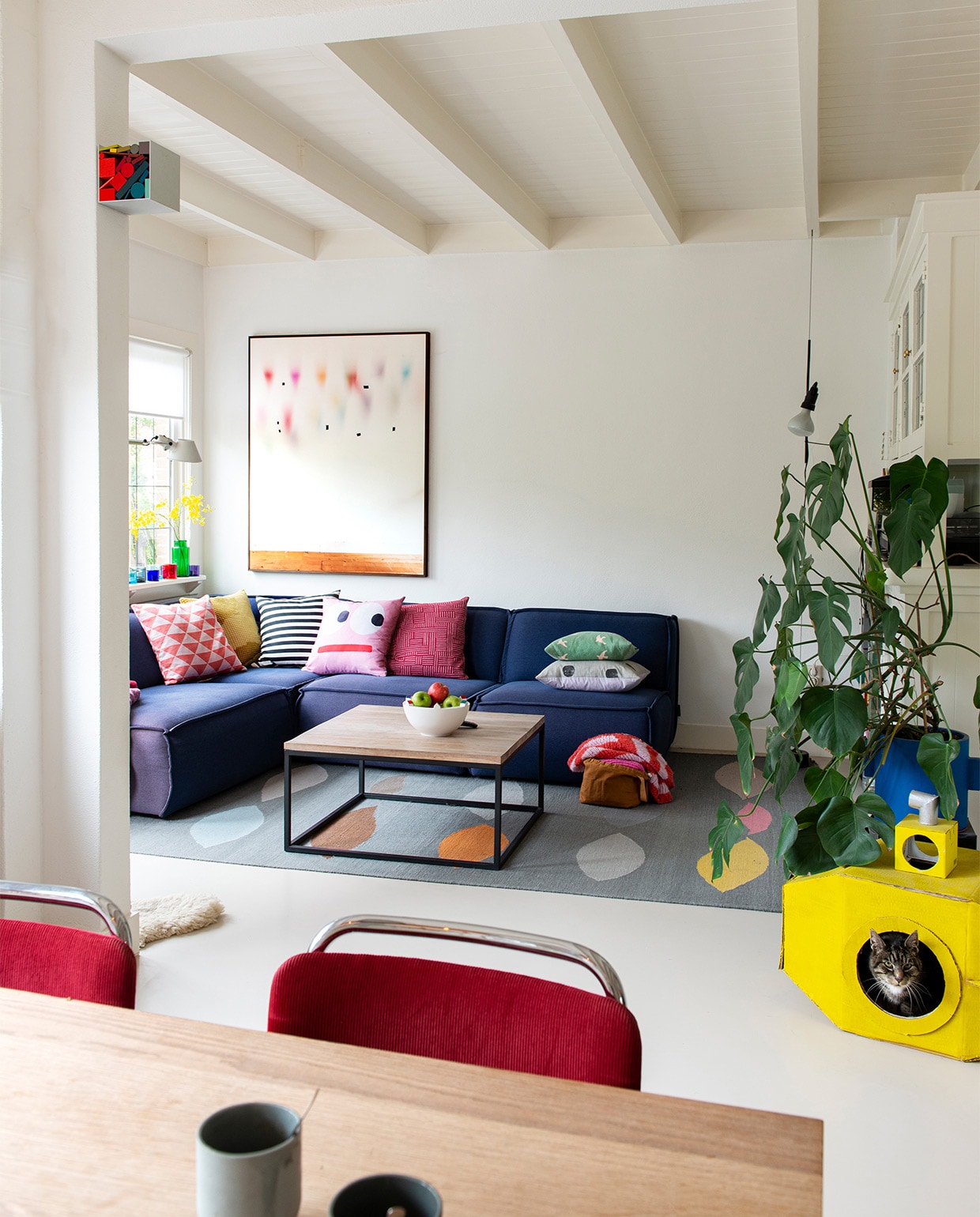 Kubus met kleuren van Sophie Smallhorn. Op de vensterbank: lamp Tolomeo van Artemide, theelichten Iittala. Bank Edge van Fest Amsterdam, kussens van diverse herkomst, fotografisch kunstwerk van Katja Mater via Galerie Heden, salontafel laten maken door smid, schaal Bebouwde Kom van Olav Slingerland, karpet Leaves van CarpetVista, in de hoek lamp Parentesi van Flos, blauwe bloempot Serax, stoelen model 101 van Gispen, op maat gemaakte eettafel Jacco Bakker, mokken De Intuïtiefabriek.
