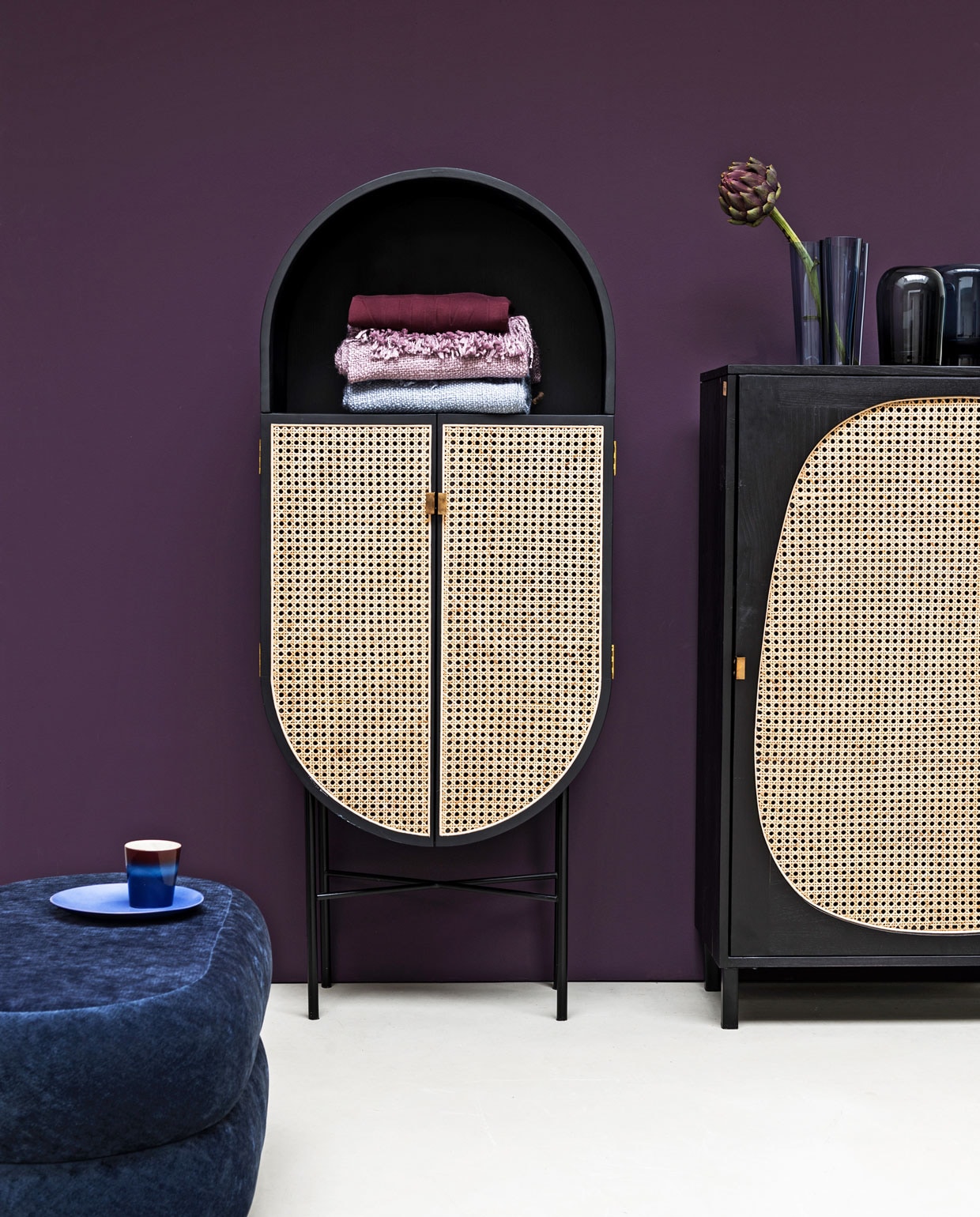 Paarse muurverf Moorland van vt wonen, (karwei.nl). Kasten Retro Oval en Retro Webbing, beide van hout, webbing en messing, blauw bord en kopje (hkliving.nl). Ovale poef van blauw velours (fermliving.com). Vaas van Ittala (links) en vaas Troll van Menu (vtwonen.nl). Plaids, (malagoon.com). Purper sweater (nike.com).