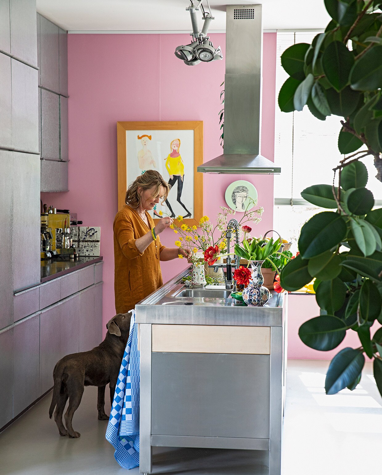 Karen aan het kookeiland van rvs en eikenhout. Apparatuur Smeg. Op maat gemaakte keuken met fronten van zink. Lamp Modular. Kunst Vanessa Beecroft. Wandbord meegenomen uit Australië. Roze muurverf Histor S0540-R30B. Overig herkomst onbekend.