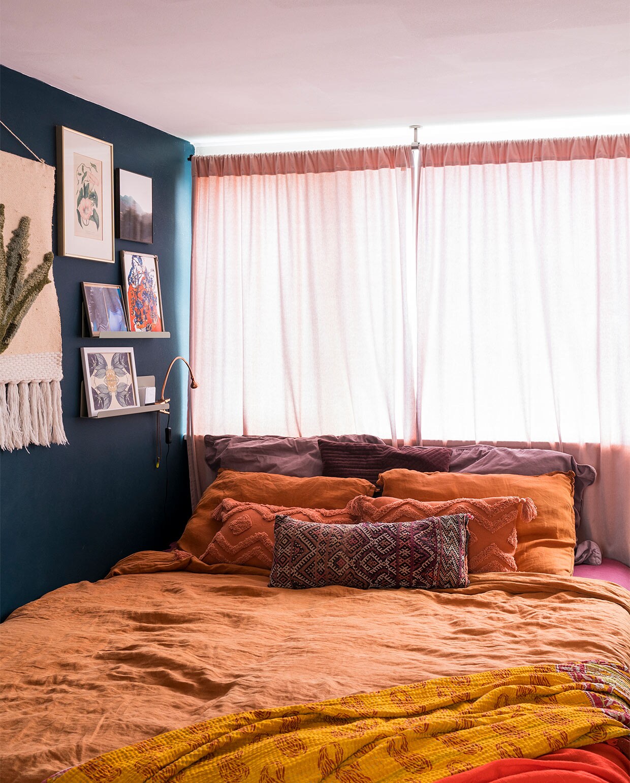 Verfkleur op de wand Hague Blue Farrow &amp; Ball. Plankjes Søstrene Grene. Wandkleed Sissy-Boy. Prent met bloemen kringloopwinkel. Landschap IrisDorine. Foto privébezit. Oranje prent maakster onbekend. Onderste prent Hanneke van de Pol. Klemlampje Ikea. Gordijnen H&amp;M Home. Terracottakleurig beddengoed La Redoute. Terracottakleurige kussens met motief Hema. Geborduurd kussen uit Marokko. Grote kussens Dille &amp; Kamille. Geribbeld kussen Hema. Kanthakleed uit India. Rode sjaal Scotch &amp; Soda.