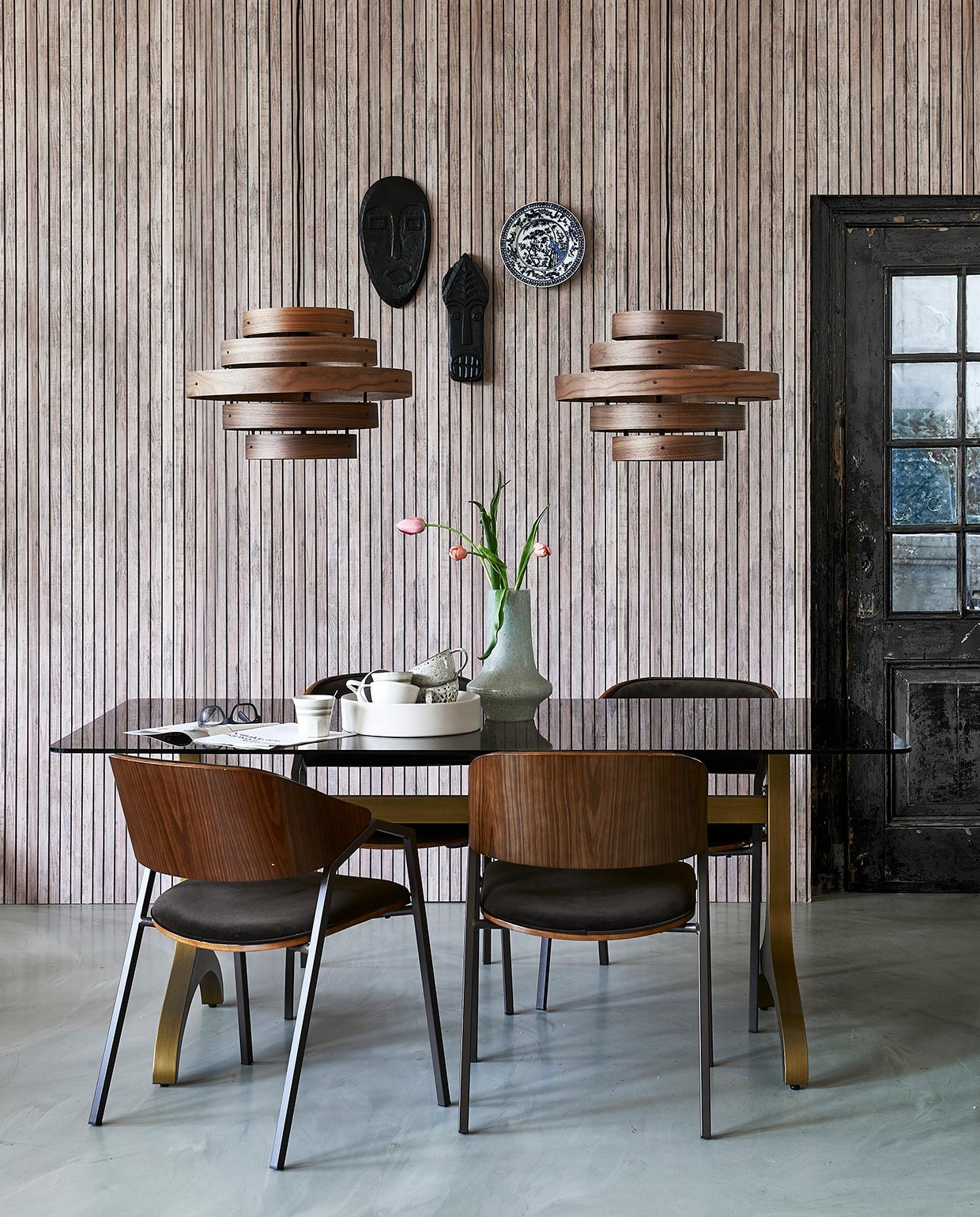 Vliesbehang met lattenprint van vtwonen (karwei.nl). Glazen tafel Sansa met messing onderstel, 180x90x75 cm (lxbxh) (dutchbone.com). StoelenClan, maskers Xara en Xavi, vaas (basiclabel.nl). Bord aan wand Kyoto, mok met streep(hkliving.nl). Walnoothouten hanglampen van Eth, 50 cm (Ø) (vtwonen.nl). Witte schaal Dixon op tafel, 32,8×7,8 cm (Øxh) (festamsterdam.com). Mokken in schaal (hm.com).