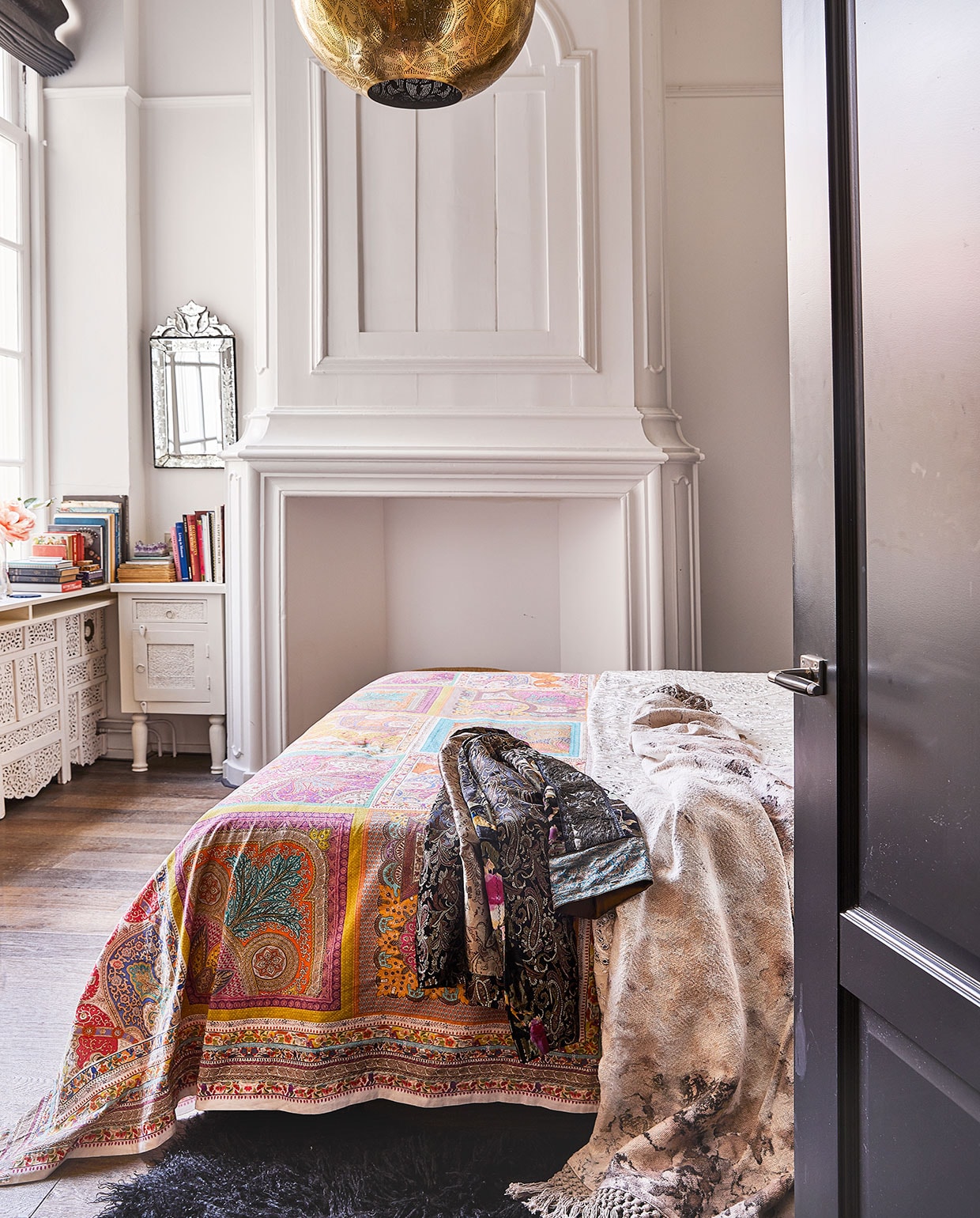 Kleurig tafelkleed van Zara Home als , sprei op bed. Kimono zelfgemaakt, sprei , van gemarmerd katoen uit India. Lamp en kastje, waar Karin zelf nog poten onder zette, Zenza. Venetiaanse spiegel van , een rommelmarkt. Schouw origineel. Radiatorombouw zelfgemaakt met een Indiaas kamerscherm.