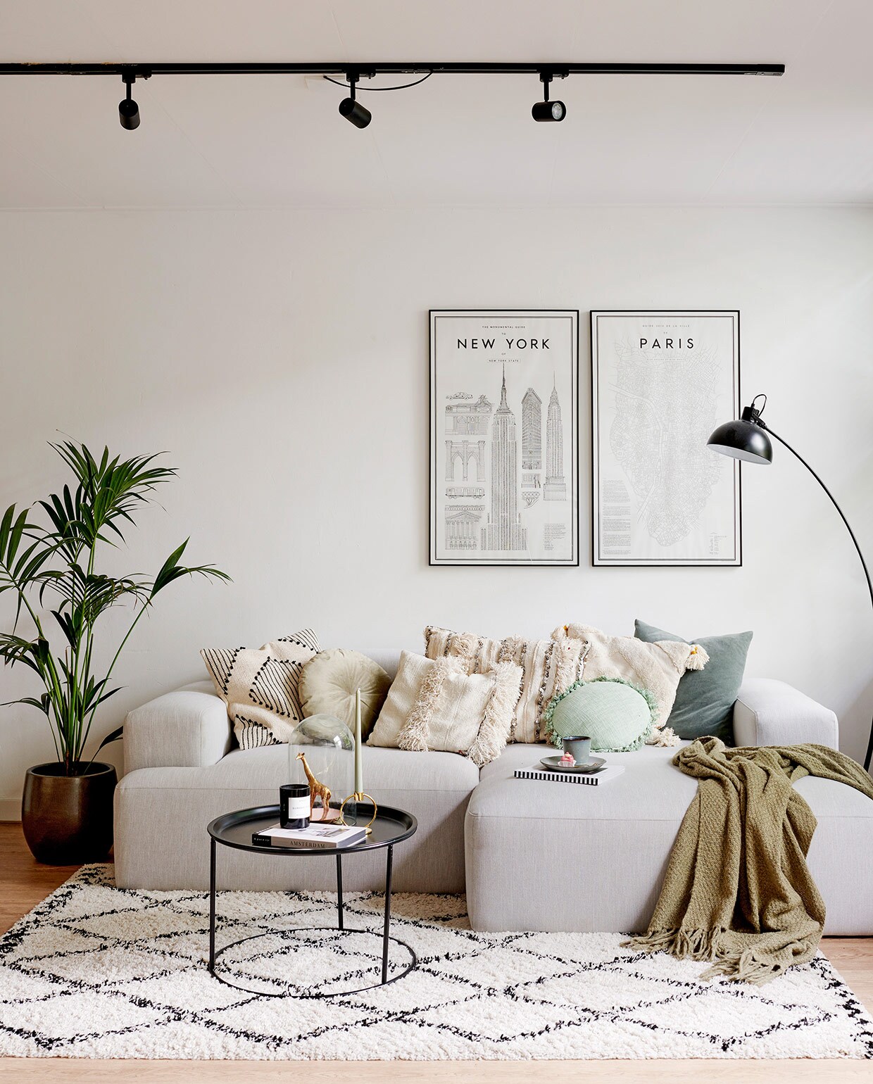 Bank Westwing, zwart-wit kussen en twee groene kussens H&amp;M Home, rond kussen Jysk, drie witte kussens The Weavery Shop, plaid Jysk. Vloerkleed en bijzettafel Karwei. Kandelaar Living-in By Romy’s. Stolp en giraffe Action. Geurkaars Skins Cosmetics. Zwarte vloerlamp herkomst onbekend. Spots plafond lampenlicht.nl. Posters My Guide To New York en Parijs van David Ehrenstråhle, myguideto.se.