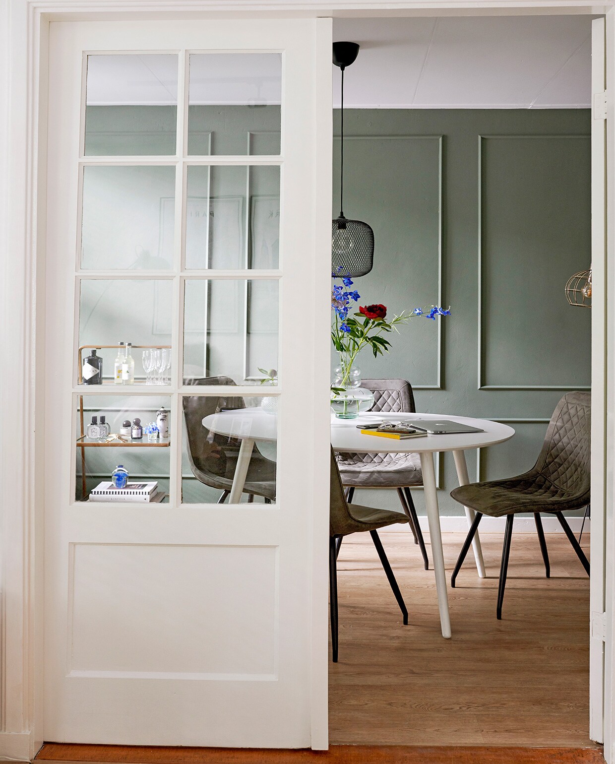 Serveerrek en glazen Living-in By Romy’s. Tafel Made. Stoelen Zitmaxx. Hanglamp Ikea. Dienblad op tafel herkomst onbekend, geurkaars in potje Fornasetti, glazen vaas Living-in By Romy’s.