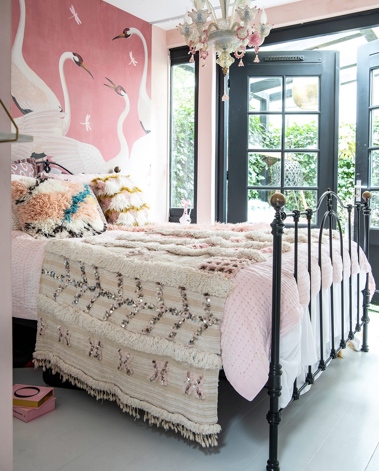 Behang kraanvogels Heron print van Gucci, vintage bed van Leeelijk. Kroonluchter van Murano-glas Antiekcentrum Amsterdam, Marokkaanse bruidssprei is een Handira via El Ramla Hamra. Kussen links van Aai Made With Love en rechts van Anthropologie. Roze kannetje in vensterbank is van Sjerpetine, gekocht op de Albert Cuyp.