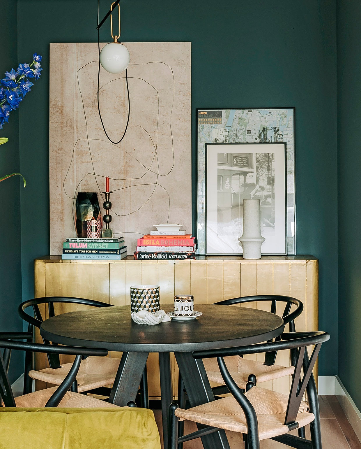 Hoge vaas Menu, bronzen bijzettafel Rapture Interior Luxury, spiegel HKliving. Muurverf Inchyra Blue van Farrow &amp; Ball. Tafel Marktplaats, stoelen Sklum, kop-en-schotel Anthropologie, wit schaaltje en zwart-wit vaasje H&amp;M Home. Dressoir Loods 5, boeken via Nox Studio Interiors en Assouline. Kandelaar, vaas en witte vaas Nox Studio Interiors. Geurkaars H&amp;M Home, schilderij en schaaltje Zara Home. Zwart-witte foto in lijst van Annes moeder geweest, lijst met poster gekocht op straat in New York. Hanglamp Artemide.