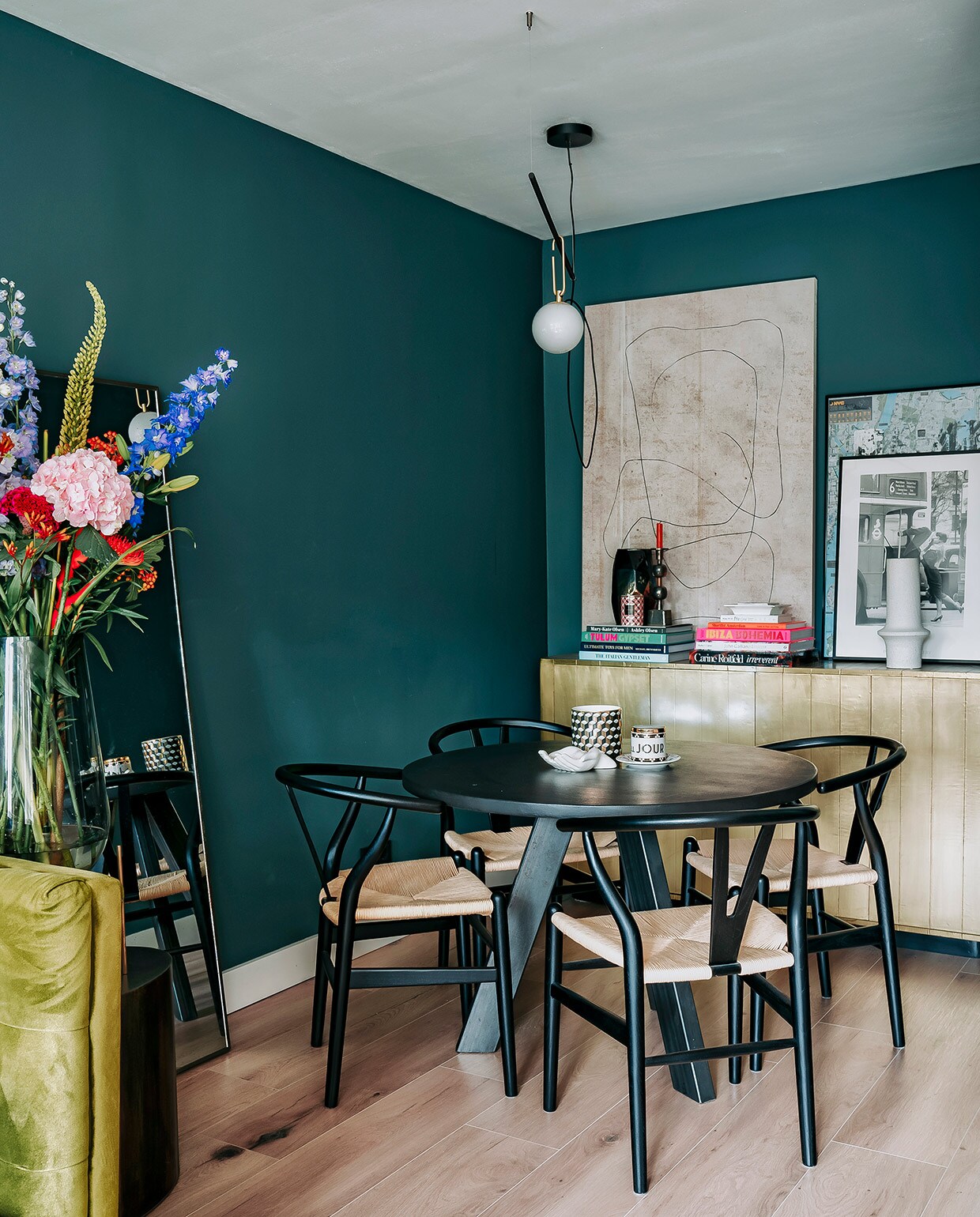 Hoge vaas Menu, bronzen bijzettafel Rapture Interior Luxury, spiegel HKliving. Muurverf Inchyra Blue van Farrow &amp; Ball. Tafel Marktplaats, stoelen Sklum, kop-en-schotel Anthropologie, wit schaaltje en zwart-wit vaasje H&amp;M Home. Dressoir Loods 5, boeken via Nox Studio Interiors en Assouline. Kandelaar, vaas en witte vaas Nox Studio Interiors. Geurkaars H&amp;M Home, schilderij en schaaltje Zara Home. Zwart-witte foto in lijst van Annes moeder geweest, lijst met poster gekocht op straat in New York. Hanglamp Artemide.