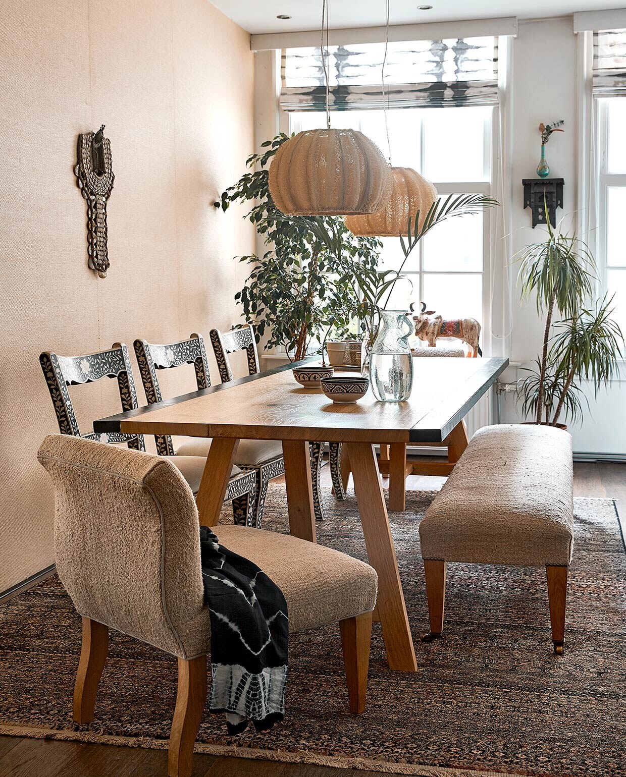 Keukentafel Heerenhuis Manufactuur, zelf verbreed. Stoelen uit India. Herkomst fauteuil en bank onbekend, bekleed met een hennepkleed uit Turkije. Op de fauteuil ligt een blouse. Zeegras behang uit Natural Wallcoverings collectie van Eijffinger. Schelpen- ornament, lampen en karaf Zenza. Wandkast uit Marokko, turquoise parfumflesvaas uit Turkije. Beeld koe souvenir uit India. Vloerkleed Dutchbone. Kommen Shabby Chic. Tie-dye raambekleding van een winkel die niet meer bestaat.