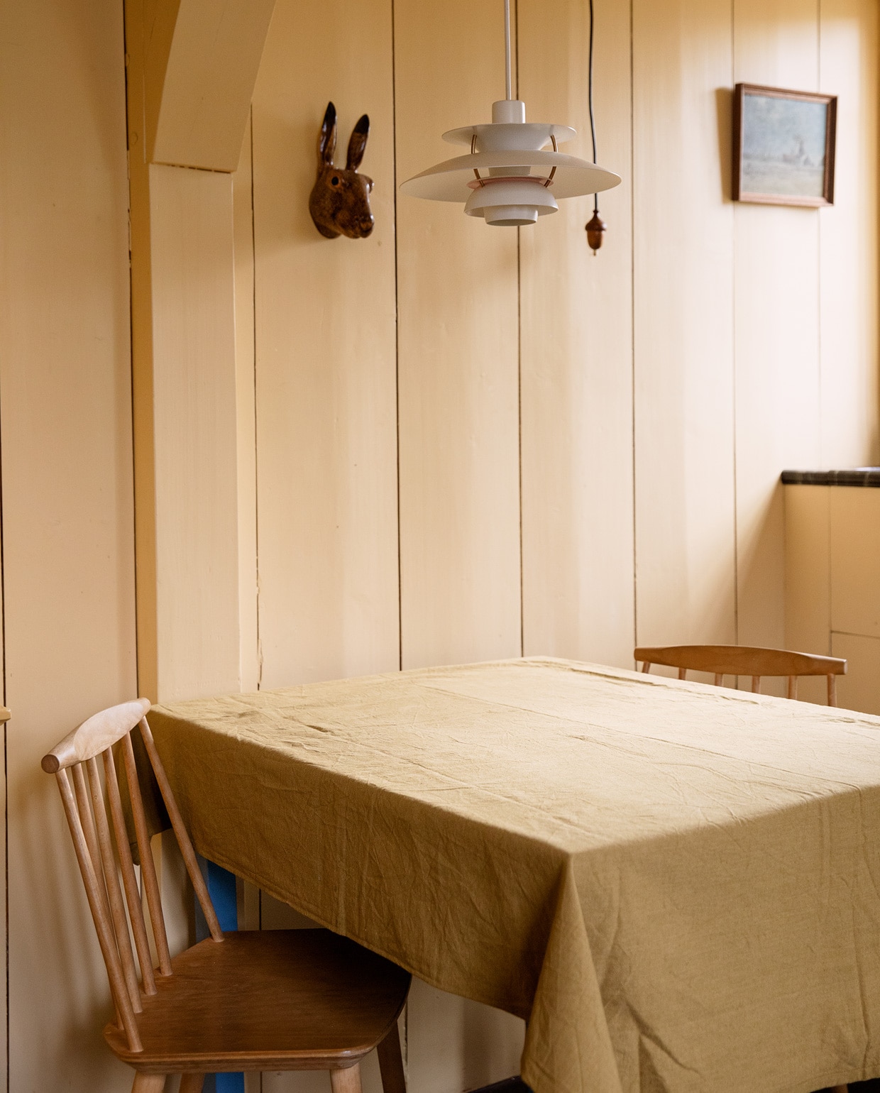 Muurverf van Aquamarijn via Rigo, kleur onbekend. Hanglamp Louis Poulsen, haas herkomst onbekend, schilderij vintage, tafelkleed Dille &amp; Kamille, stoelen Hay.