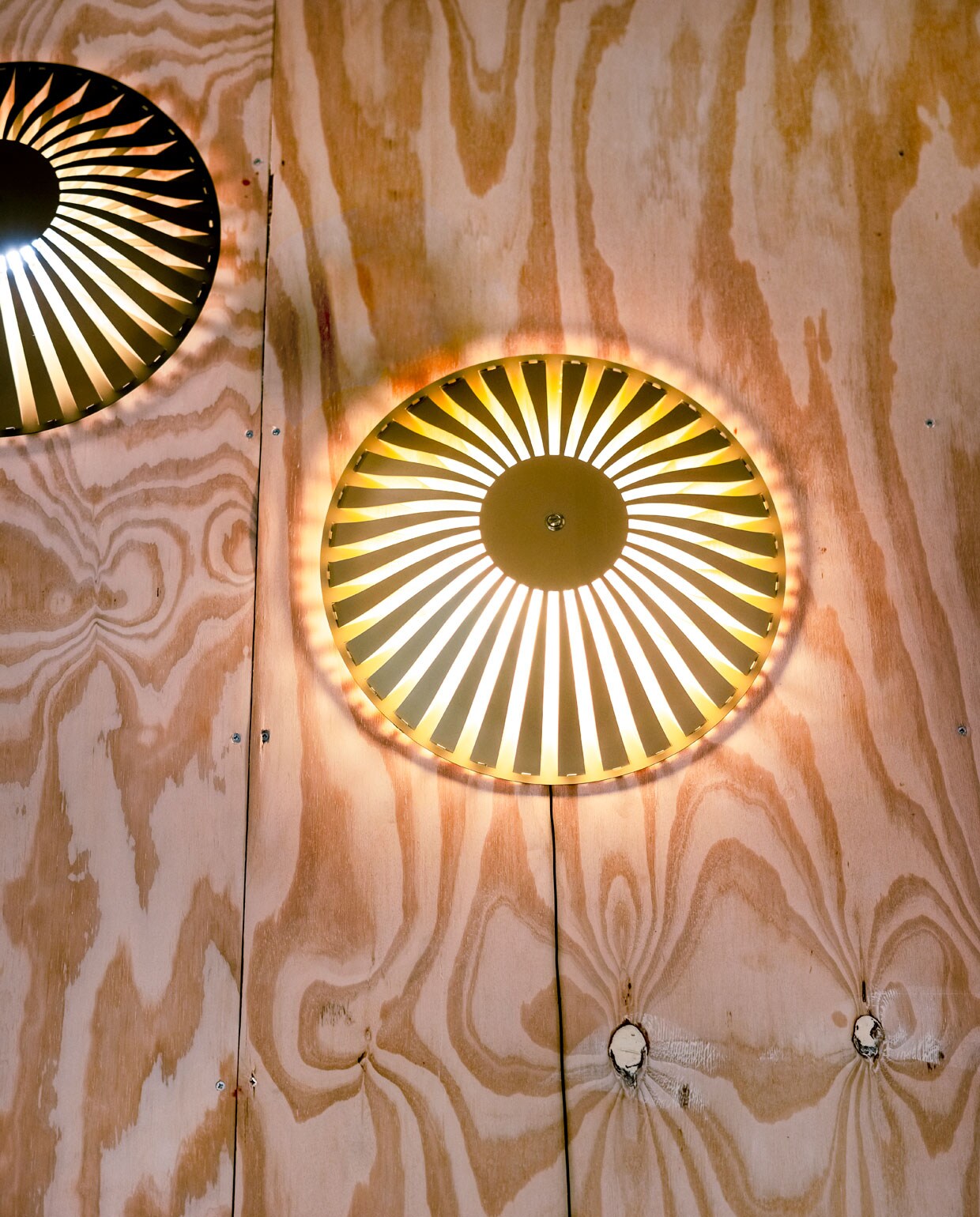Glint betekent letterlijk ‘kleine, heldere lichtflitsen produceren die door een oppervlak worden weerkaatst’. Lamp Glint, in de collectie van Vij5, doet precies dat; het reflecteert licht op de twee aluminium, in elkaar grijpende elementen, waarbij de armen elkaar overlappen en de lichtbron bedekken. Er ontstaat een poëtisch lichtspel, dat het licht verspreidt op de muren, de vloer en het plafond. Wat de behuizing van geanodiseerd aluminium zo bijzonder maakt; elke kleur heeft zijn eigen effect op de weerkaatsing van de verlichting en geeft het licht zijn eigen intensiteit en kwaliteit.