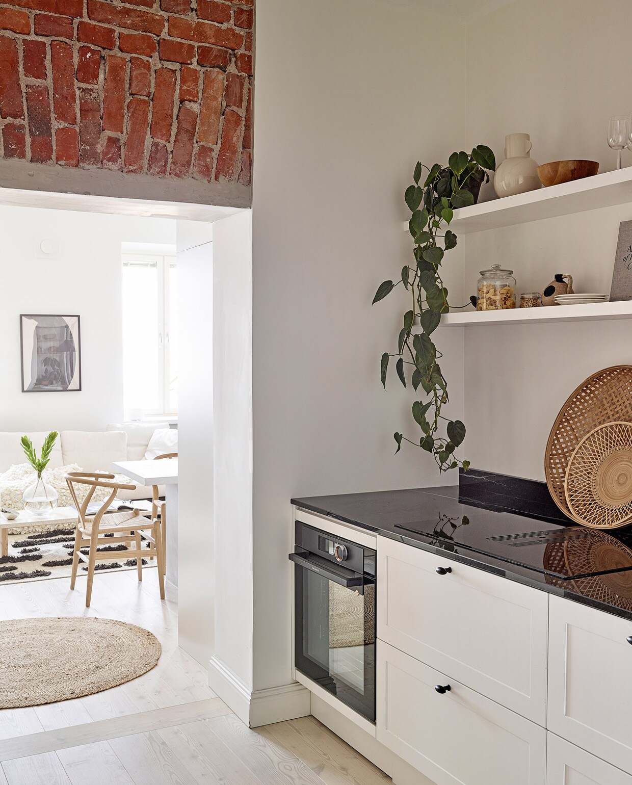 Rond vloerkleed Tine K Home. Eetkamerstoelen Wishbone Carl Hansen &amp; Son. Keuken Nixi. Beige vaas, glazen pot, witte borden en rotan dienbladen vintage. Houten kom herkomst onbekend.