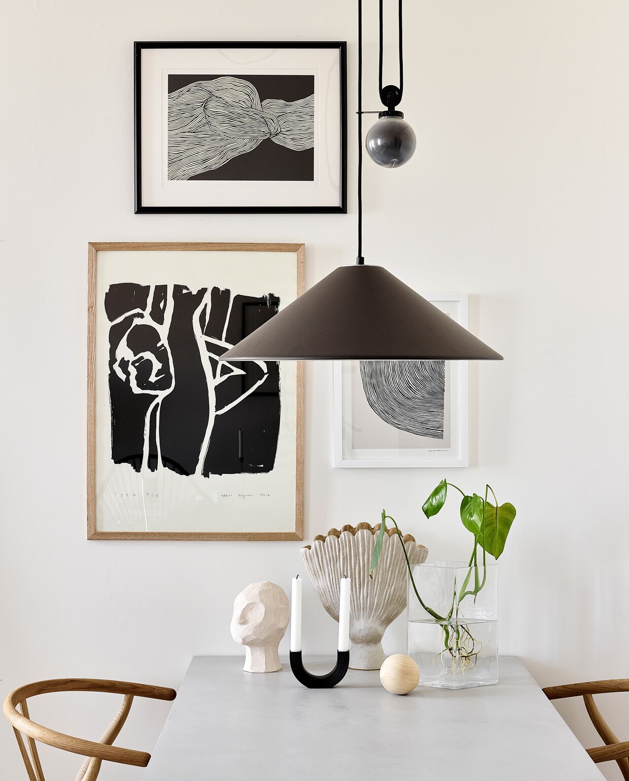 Posters The Poster Club. Eettafel Bond eigen ontwerp, verkrijgbaar via Decorativi Design. Eetkamerstoelen Wishbone Carl Hansen &amp; Son. Keramieken hoofd Kristiina Haataja, ronde kandelaar Ferm Living, keramieken vaas Samuji, glazen vaas Iittala. Hanglamp Aggregato Saliscendi Artemide.