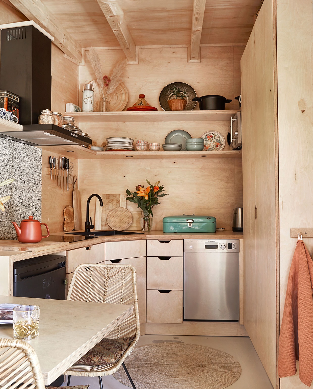Eettafel zelfgemaakt. Stoelen Van Til Outlet. Koelkast tweedehands, zwart geverfd met krijtbordverf. Theepot Xenos. Kraan Praxis. Messen, scharen, houten snijplanken herkomst onbekend. Bamboe messenhouder Duikelman. Groene broodtrommel van Carmens ouders geweest. Potten op afzuigkap Clayre &amp; Eef. Servies op de planken kringloop, rommelmarkt en van Carmens oma geweest. Thermoskan en gebloemd bord Tastoe. Vaas met droogbloemen, rieten bord, tajine herkomst onbekend. Schaal kringloop. Gietijzeren pan The White Series. Vaatwasmachine Bosch. Theedoek Kwantum.