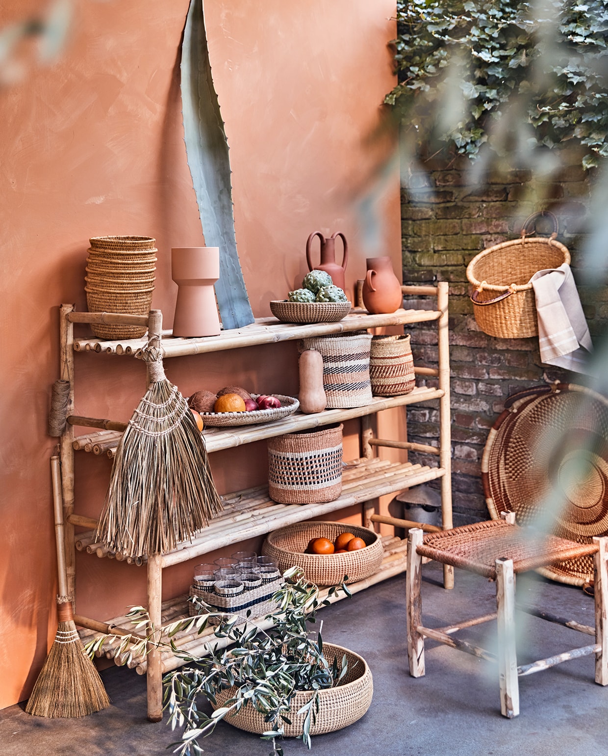 Muur geschilderd met buitenverf Kalei in Dry Terra van Pure &amp; Original, per 5 liter € 225,80 (deruamsterdam.nl). Bamboe rek van Tine K Home, 110x150x40 cm (hxlxb), olijfhouten kruk met oranje zitting, 45×45 cm, mand met hengsels, oranje sisal manden, Iraca palm schalen, mand Ghana aan de muur, platte palmblad schaal, hoge mand met ribbels Gogo (couleurlocale.eu). Terracotta vaas met oren, terracotta vaas met één oor, lichtoranje vaas (nordal.eu). Bezem, bezem met houten steel van Madam Stoltz (deens.nl).