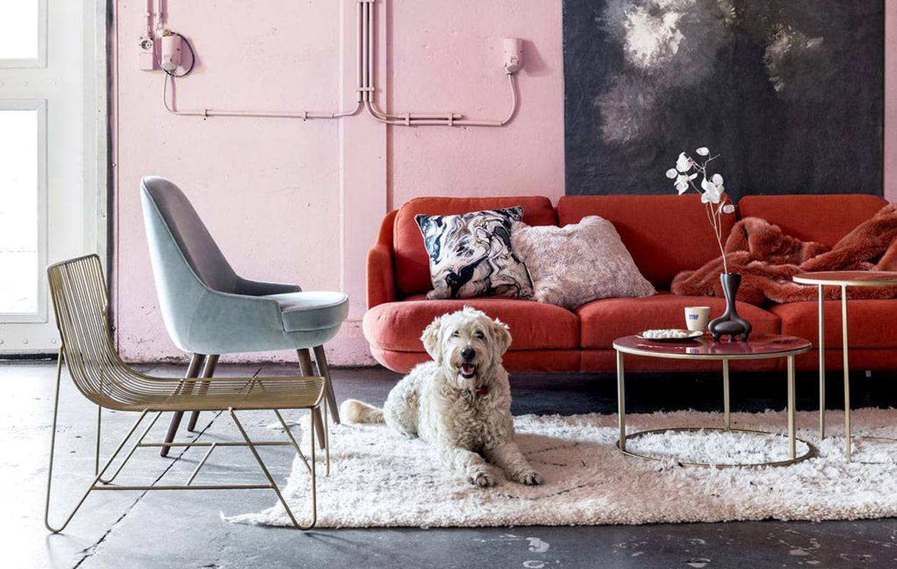 Lune 3-zitsbank, ontworpen door Jaime Hayón voor Fritz Hansen, fauteuil in zeegroen fluweel ontworpen door Walter Knoll (Mister Design). Kussen met marmereffect van Nordal (vtwonen.nl). Kussen van nepbont en plaid van nepbont (Padcon). Messingkleurige draadstoel van Madam Stolz (deens.nl). Tafels, vloerkleed (Pols Potten). Canvas doek met kreukeffect met kopie van schilderij Stilleven met Bloemen van Auguste Jouve uit de collectie van het Rijksmuseum (More than Canvas). Vaas in samenwerking met Roderick Vos, mok in samenwerking met Edwin Vollebergh (Social Label).