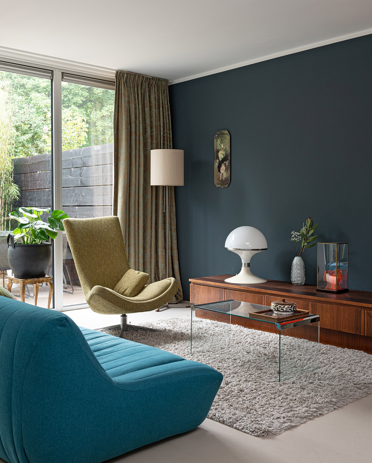 Muurverf Deep Ocean van Histor, gordijnen van de moeder van Charlotte. Staande lamp, tafel tweedehands. Plantenpot Household Hardware. Draaistoel Rudolf Wolf. Bank Made. Kleed Shaggy van Trendcarpet. Marmoleumvloer Walton Forbo vloeren. Dressoir vintagevirus.nl. Lamp Concept van Brabantia. Op het dressoir: middelste vaas kringloop-winkel. Object rechts eigen ontwerp. Portret in vitrine HKliving. Glazen tafeltje Marktplaats. Keramieken bakje, dienblad vintage. Plateau madeindesign.com .